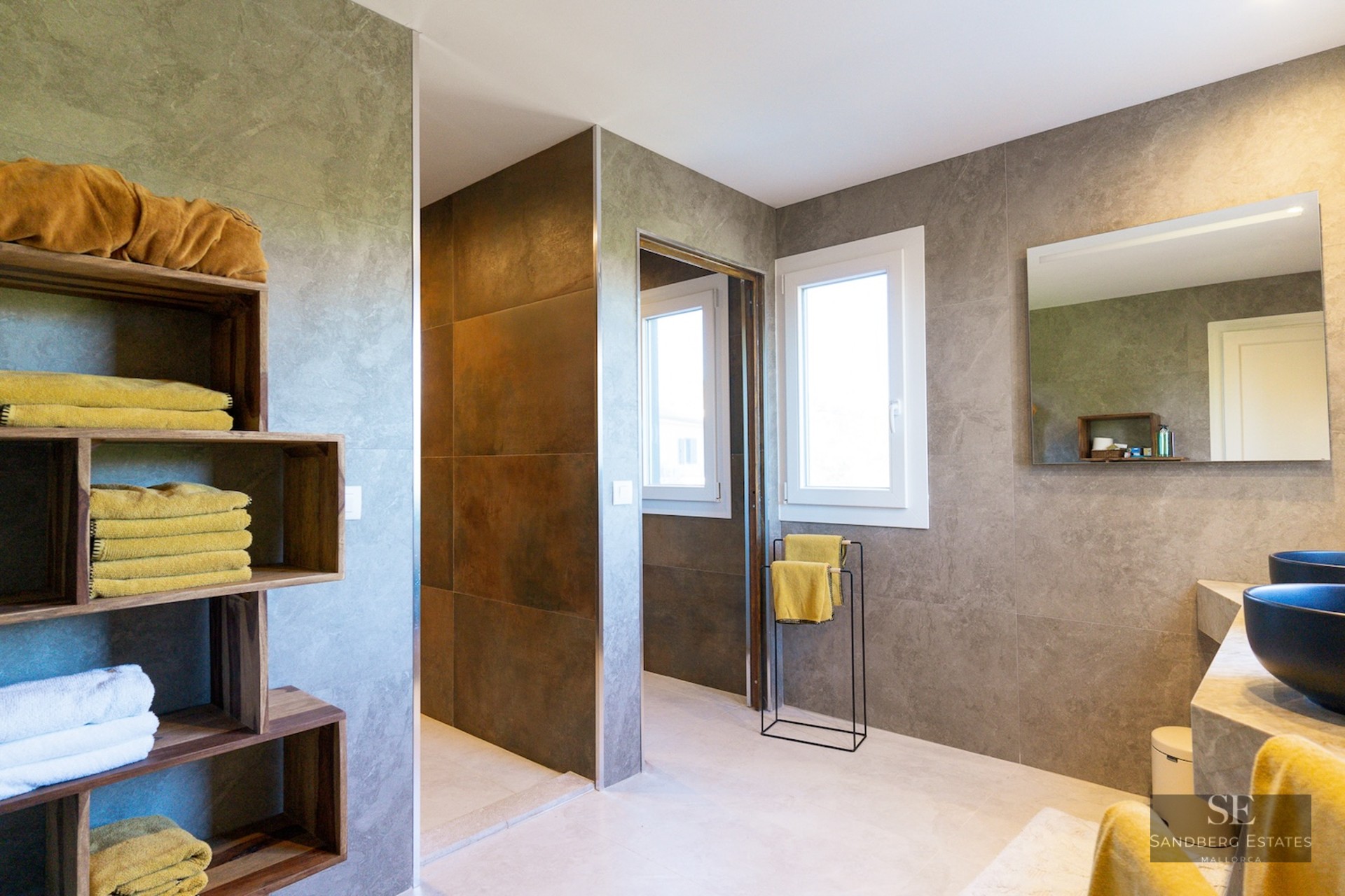 Modern bathroom featuring gray stone walls, wooden cubby shelves with yellow towels, and black vessel sinks.