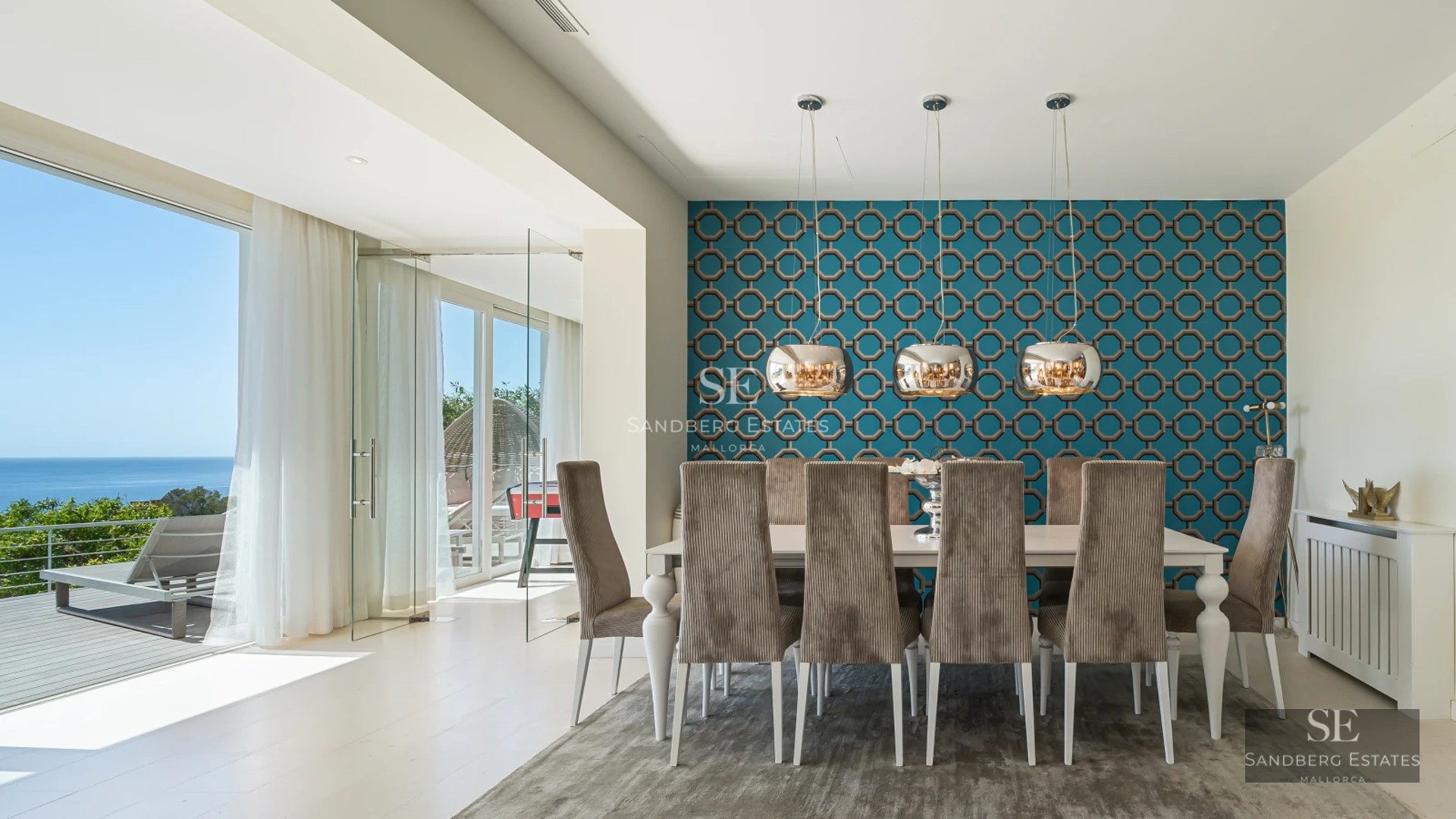Wide view of bright living room with balcony and sea view. Modern furniture in neutral tones. Light wood flooring.