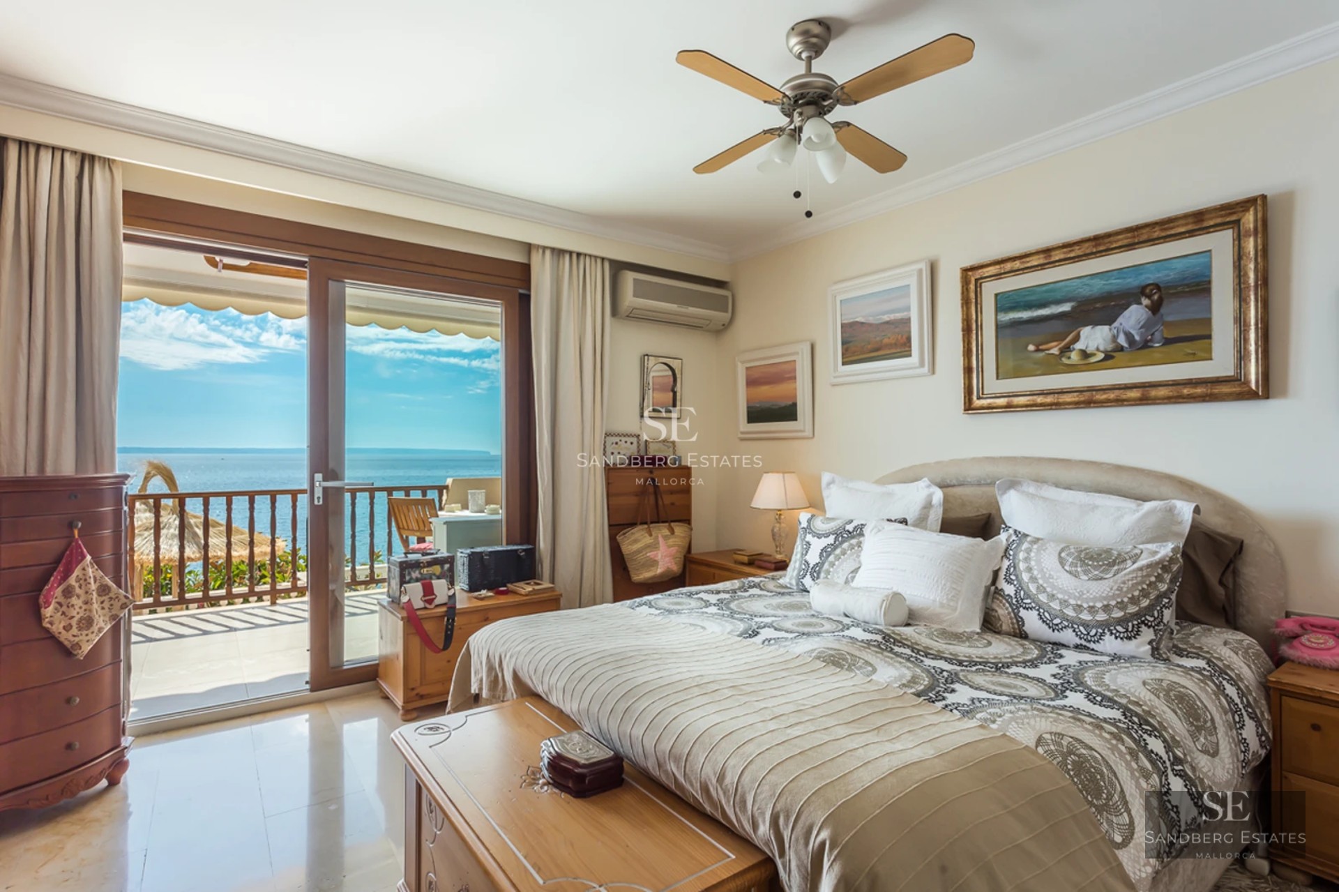 A bright master bedroom with patterned bedding and sliding glass doors opening onto a balcony with an expansive sea view.