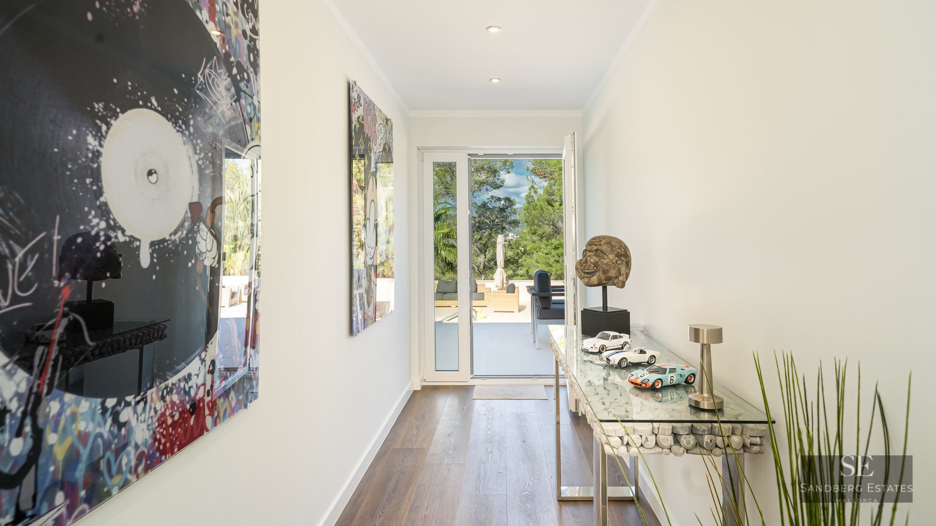 Couloir moderne lumineux avec du pop art vibrant, une console en verre et une porte ouverte sur une terrasse arborée.