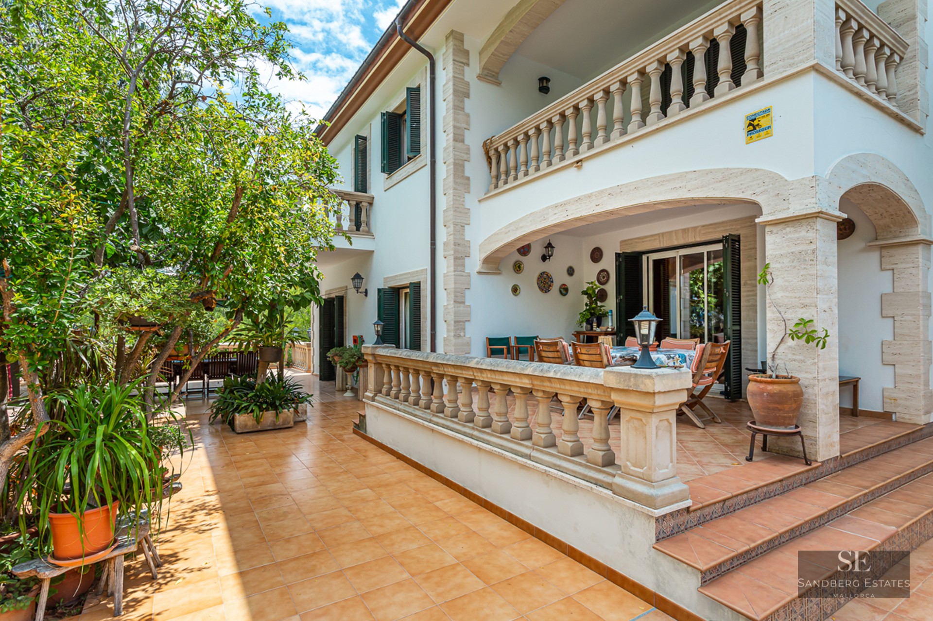 Terracotta tiled terrace with stone balustrades, shaded dining area, and lush green trees.