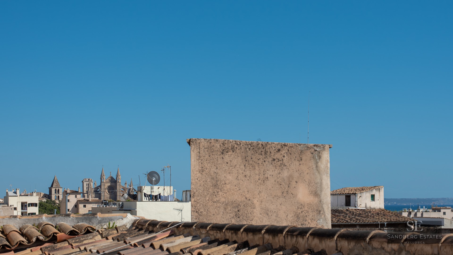 View from a tiled rooftop overlooking a historic Mediterranean city with a large Gothic cathedral under a clear blue sky.