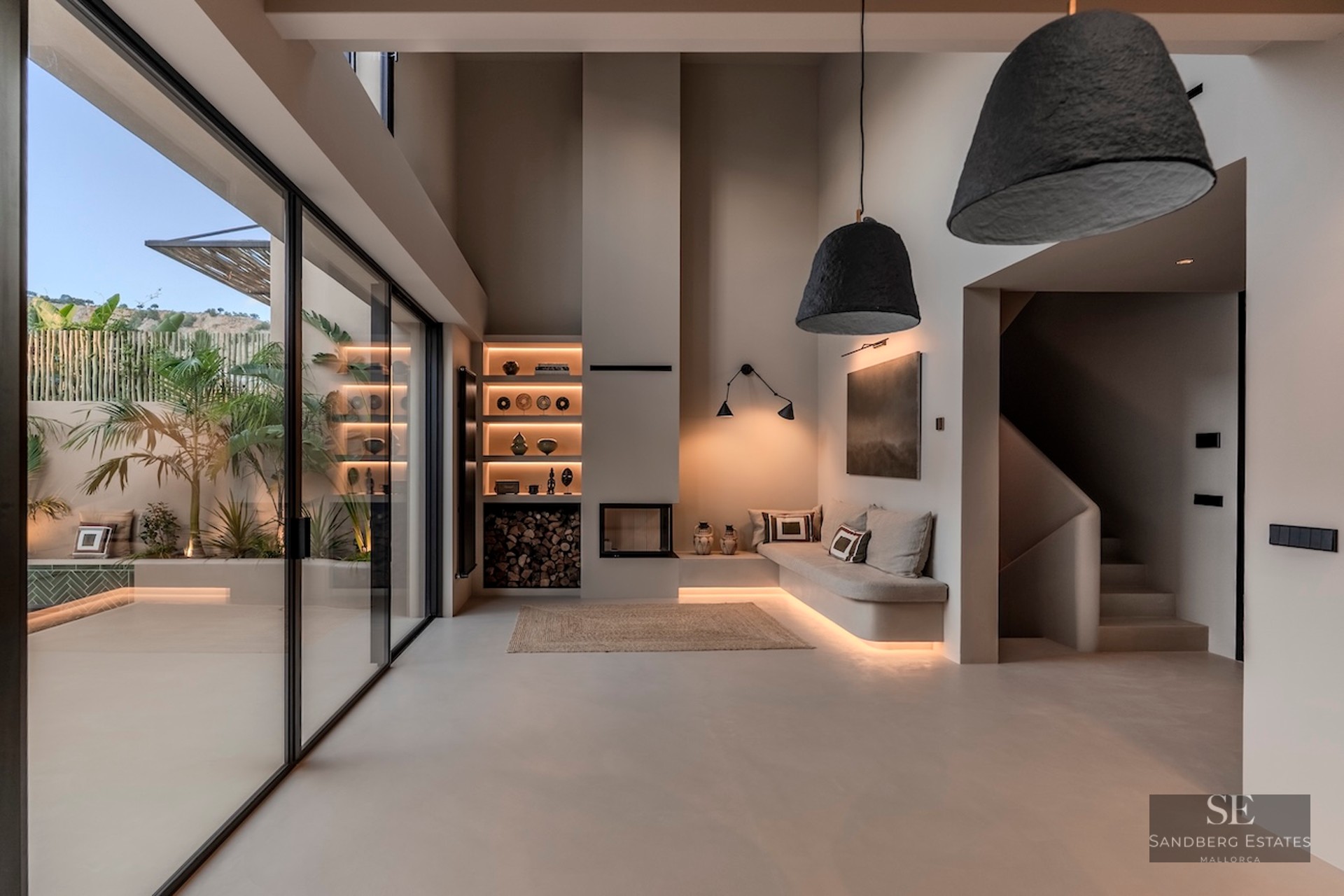 Salon minimaliste avec de hauts plafonds, un canapé intégré, une cheminée et de grandes baies vitrées sur un patio tropical.