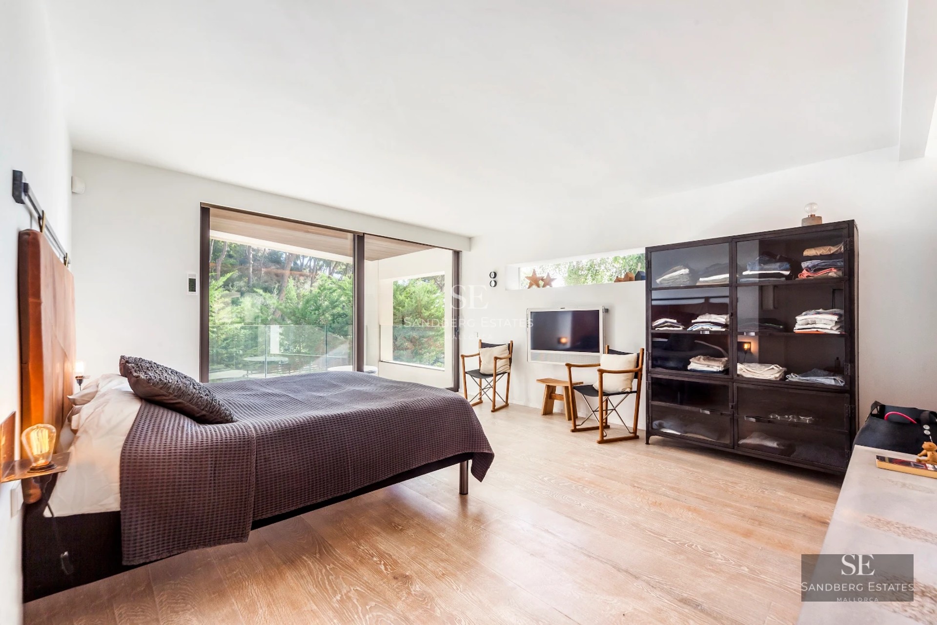 View of infinity pool with wood edge and sun loungers, surrounded by vegetation. Modern architecture with large windows.