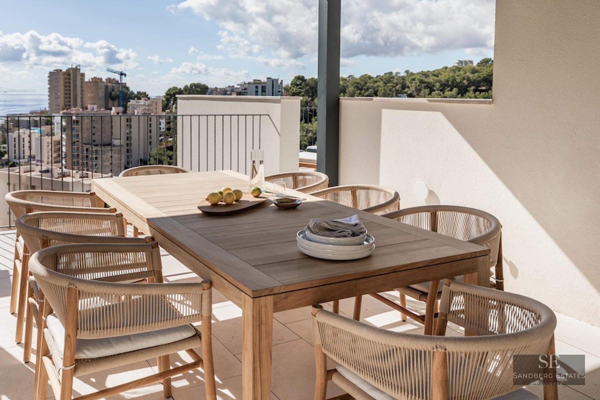 Modern outdoor dining area on a terrace featuring a wooden table, woven chairs, and a panoramic sea view.