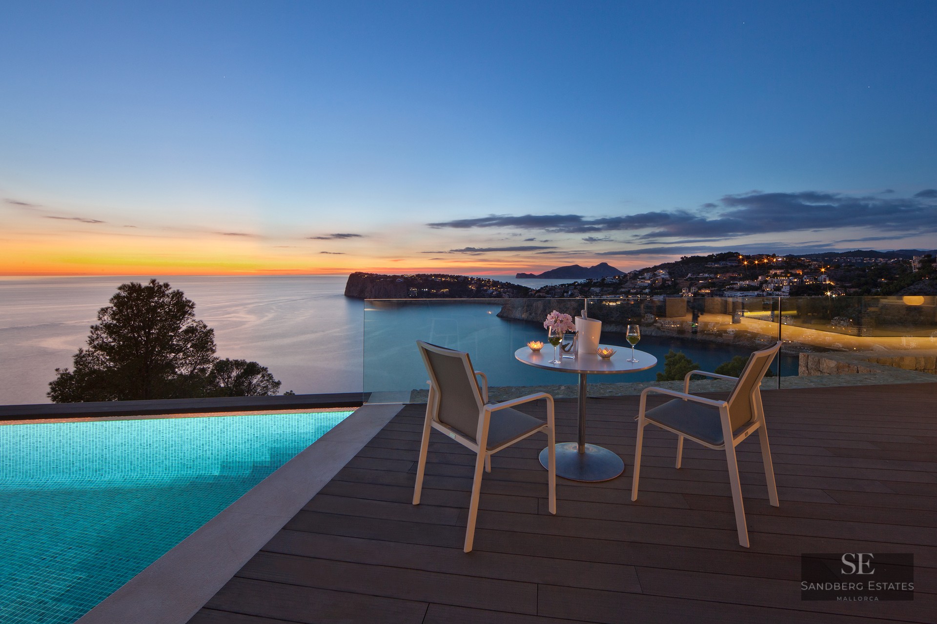 Luxury terrace with infinity pool, table for two, and panoramic sea view at sunset.
