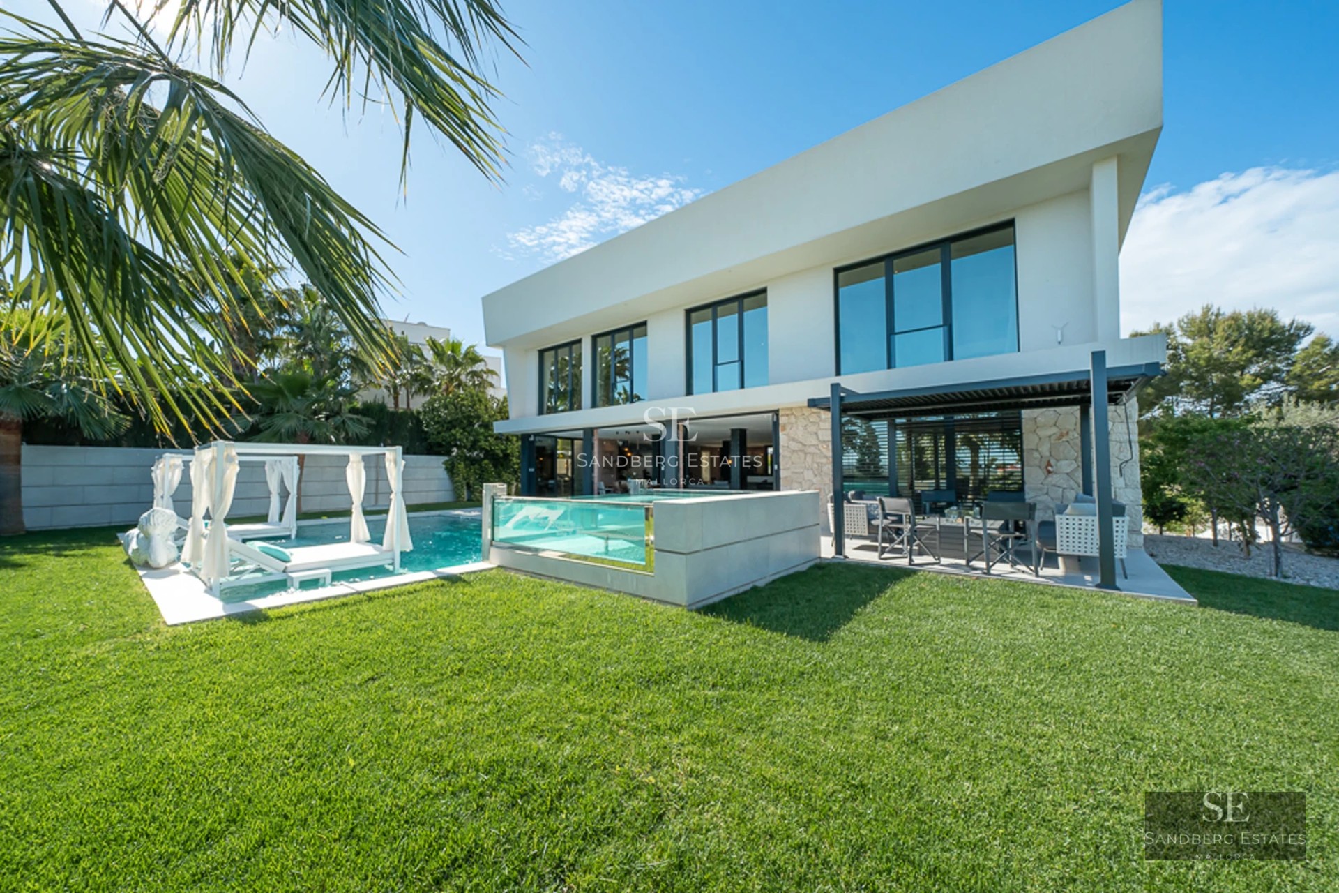 Spacious living room with panoramic windows, ocean view, light wood floors, fireplace, and modern furniture in neutral tones.