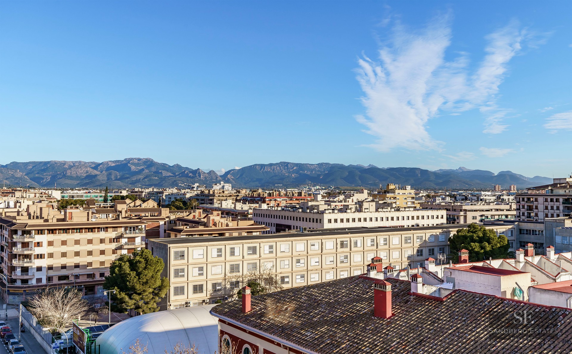 Elevated view over city rooftops towards a distant mountain range under a clear blue sky.