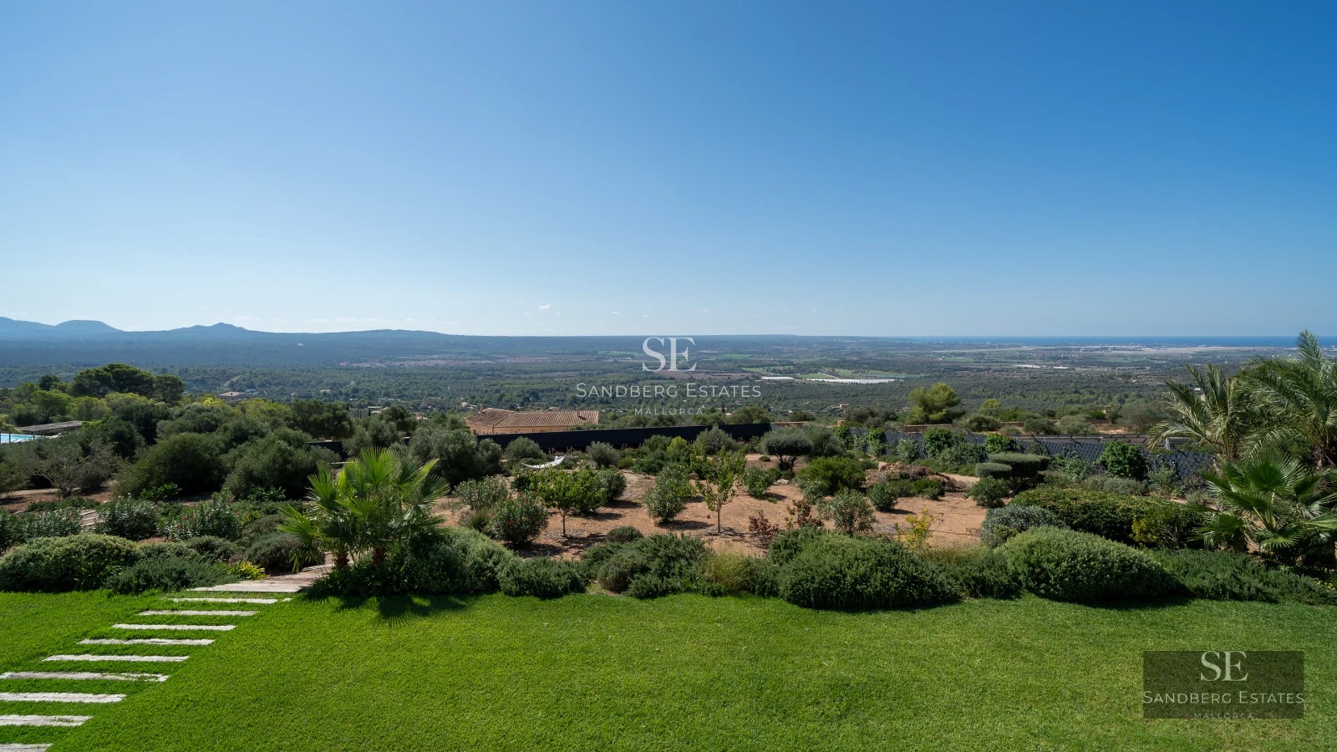 View of infinity pool with loungers and lush garden. Modern architecture with large windows and clear sky.