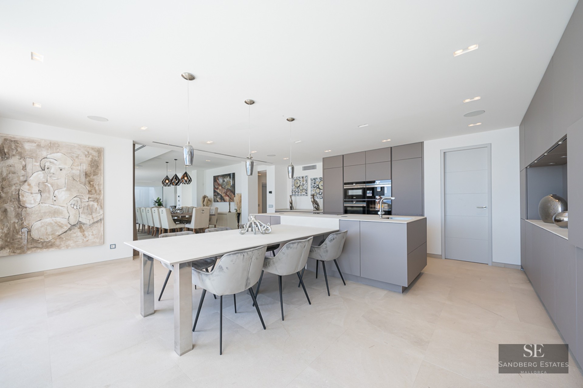 Modern kitchen with grey cabinetry, white island with attached dining table and grey velvet chairs.