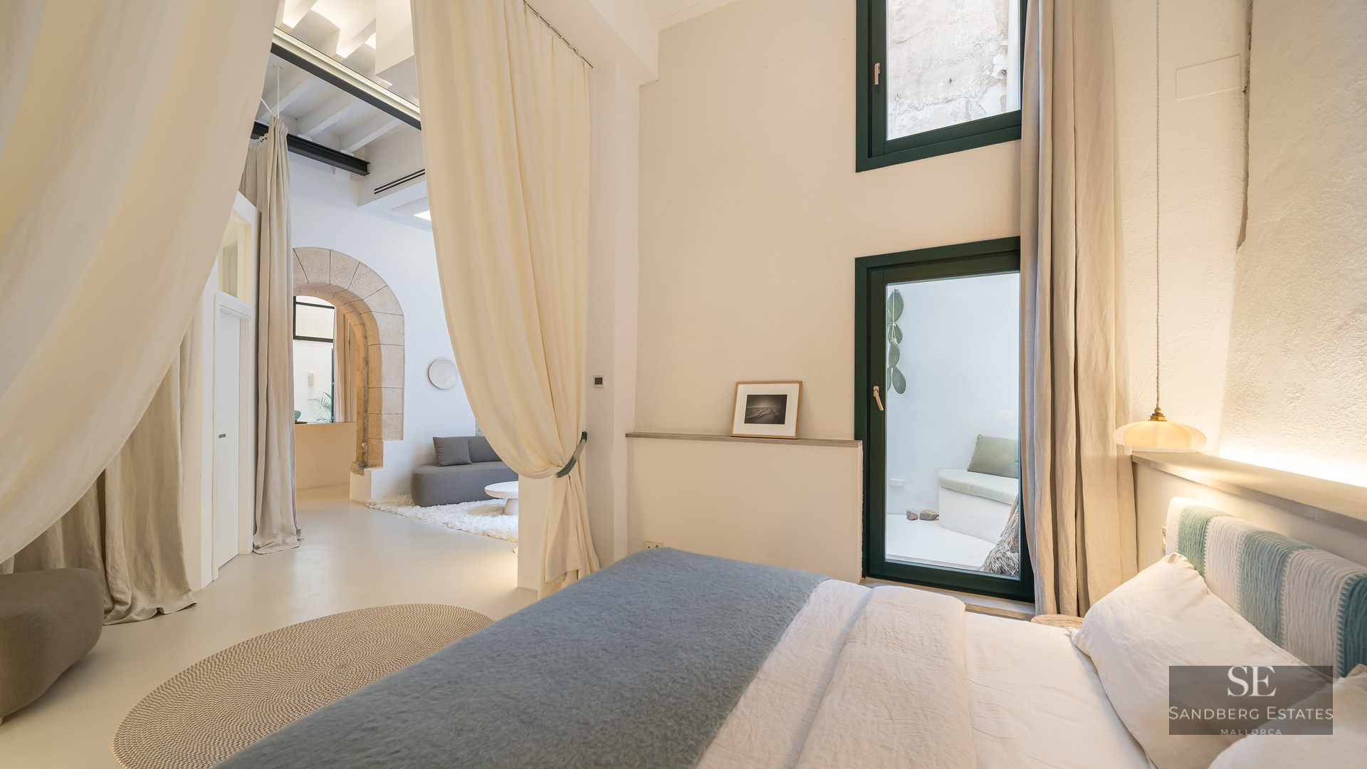 Luxury bedroom with bed, cream curtains, a stone arch, and a view of a private patio.