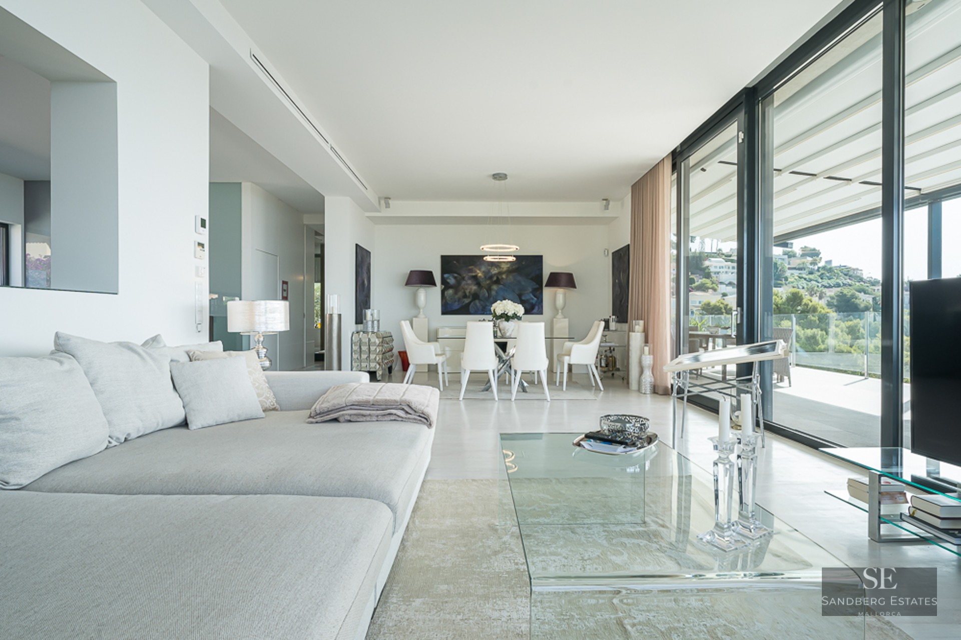 Bright, modern living room featuring a grey sectional sofa, glass coffee table, and floor-to-ceiling windows with views.