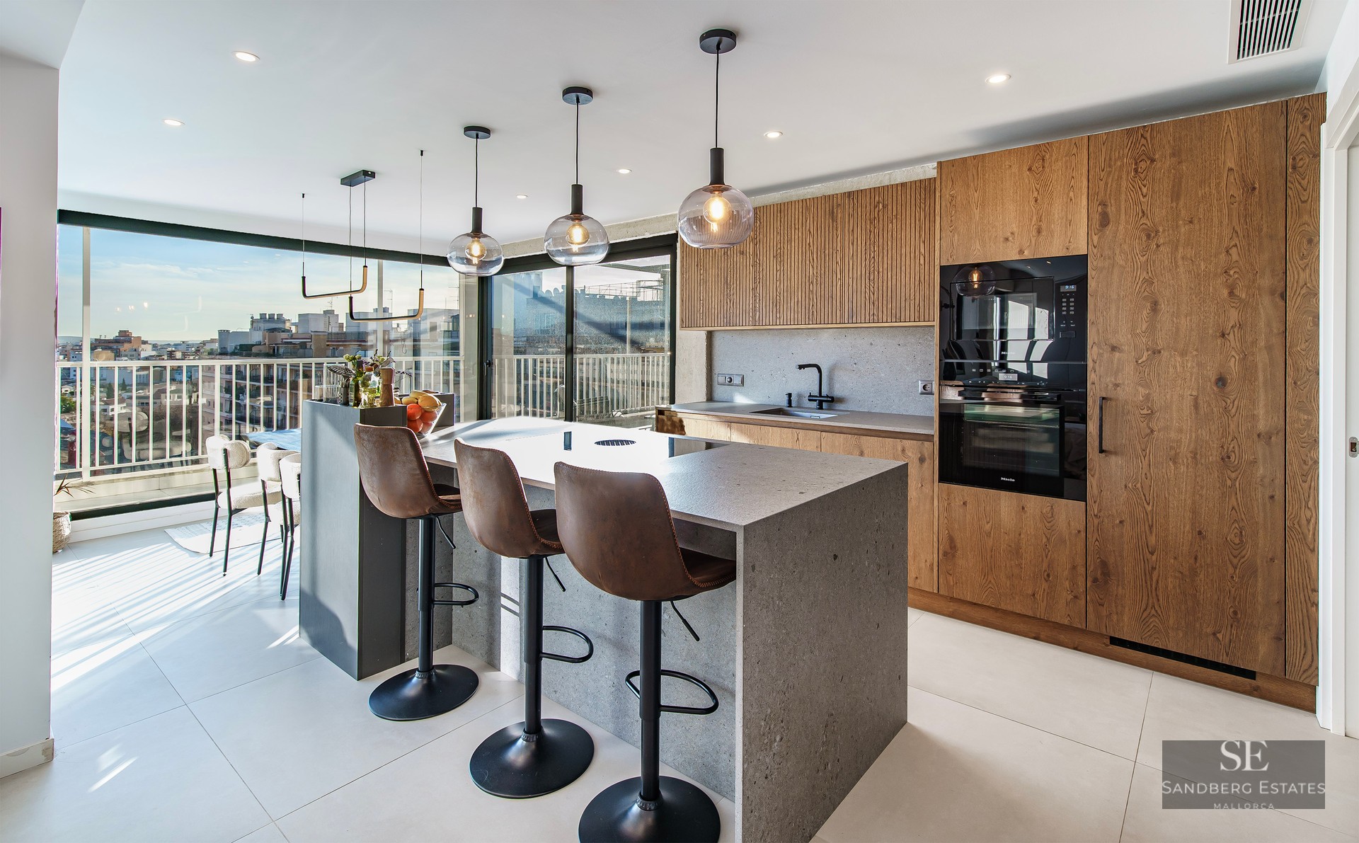 Modern kitchen featuring a stone island with three leather stools, wood cabinetry, and large windows with urban views.