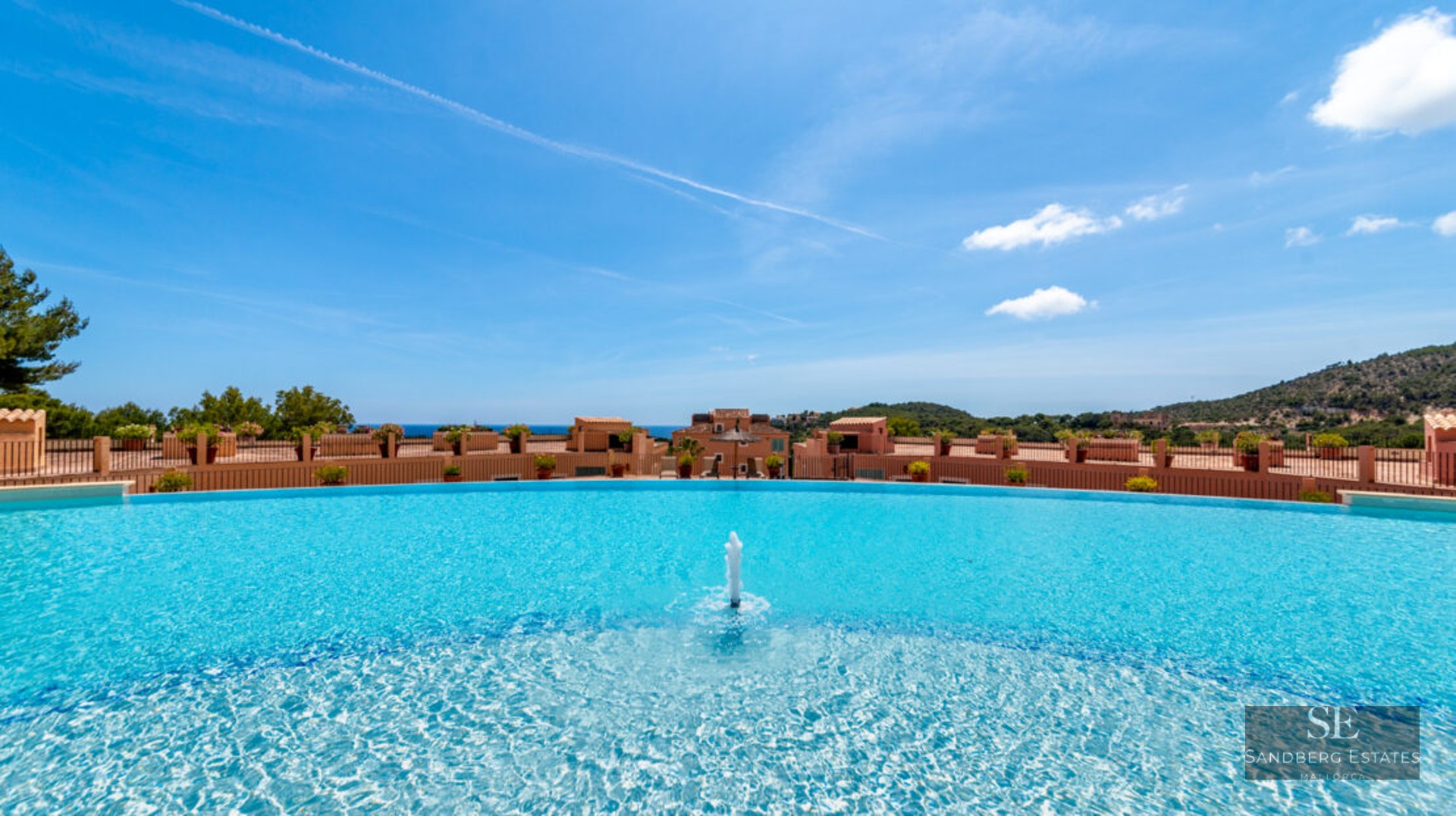 Grande piscine incurvée avec fontaine centrale et vue panoramique sur les bâtiments méditerranéens et la mer.