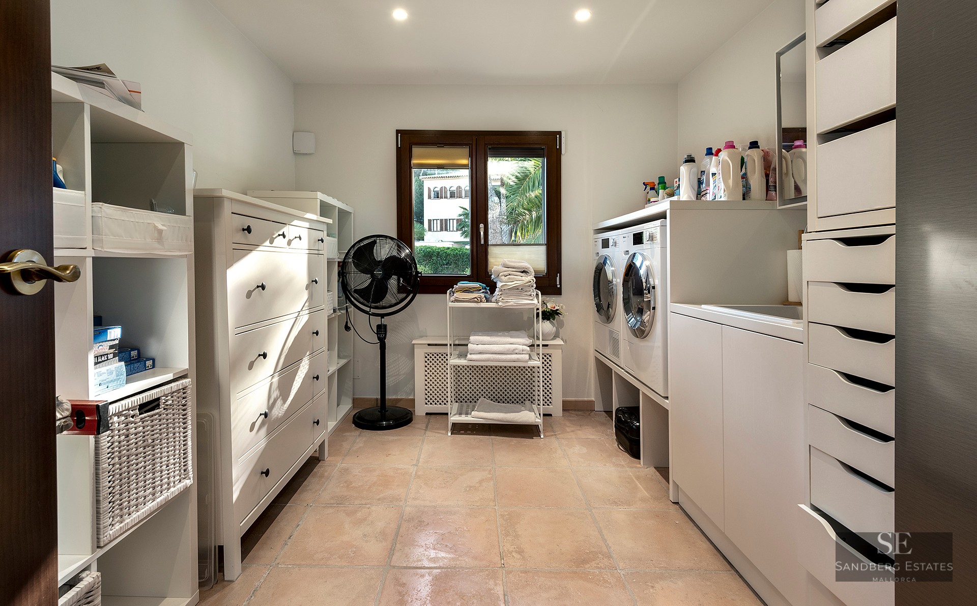 Clean laundry room with white cabinetry, washer, dryer, and terracotta tile flooring under natural light.