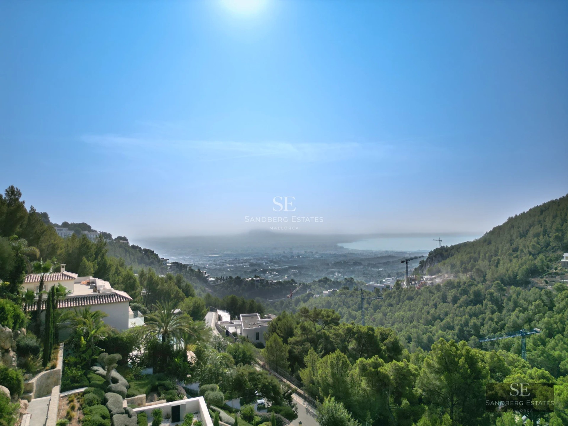 Exterior view of a luxurious modern house with an infinity pool, large windows, and lush landscaping.