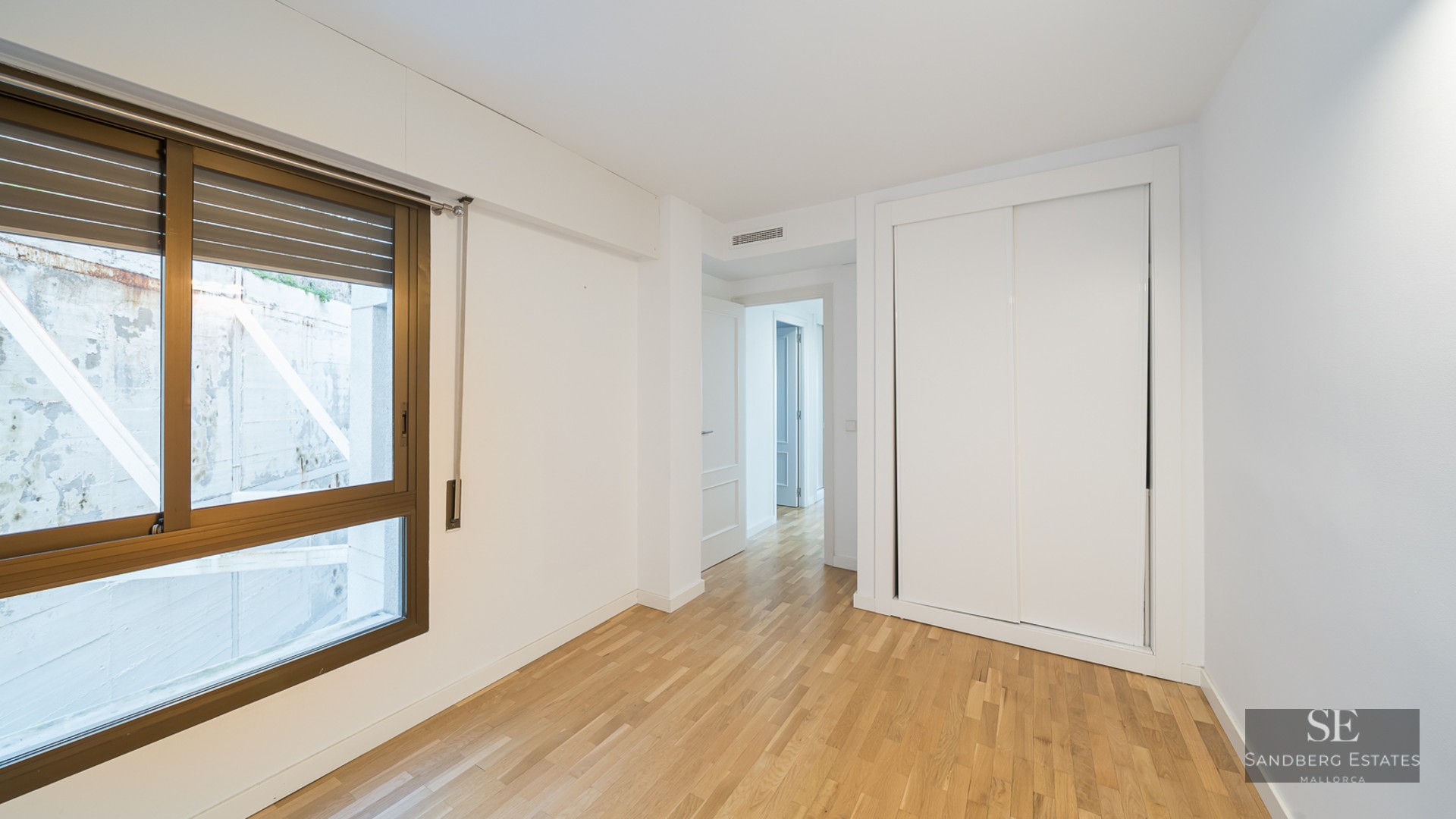 Empty room with light wood floors, a white built-in sliding door closet, and a large window with a bronze frame.