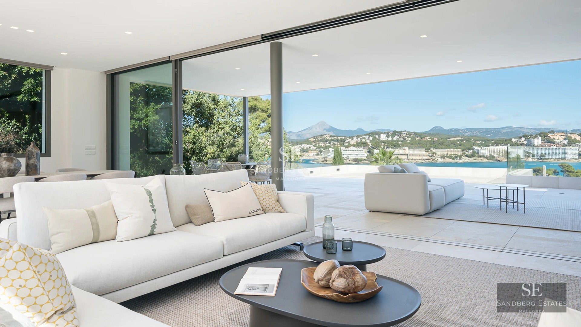 Exterior of a modern villa with an infinity pool, sun loungers, and spacious green areas. Minimalist architectural design with large windows.
