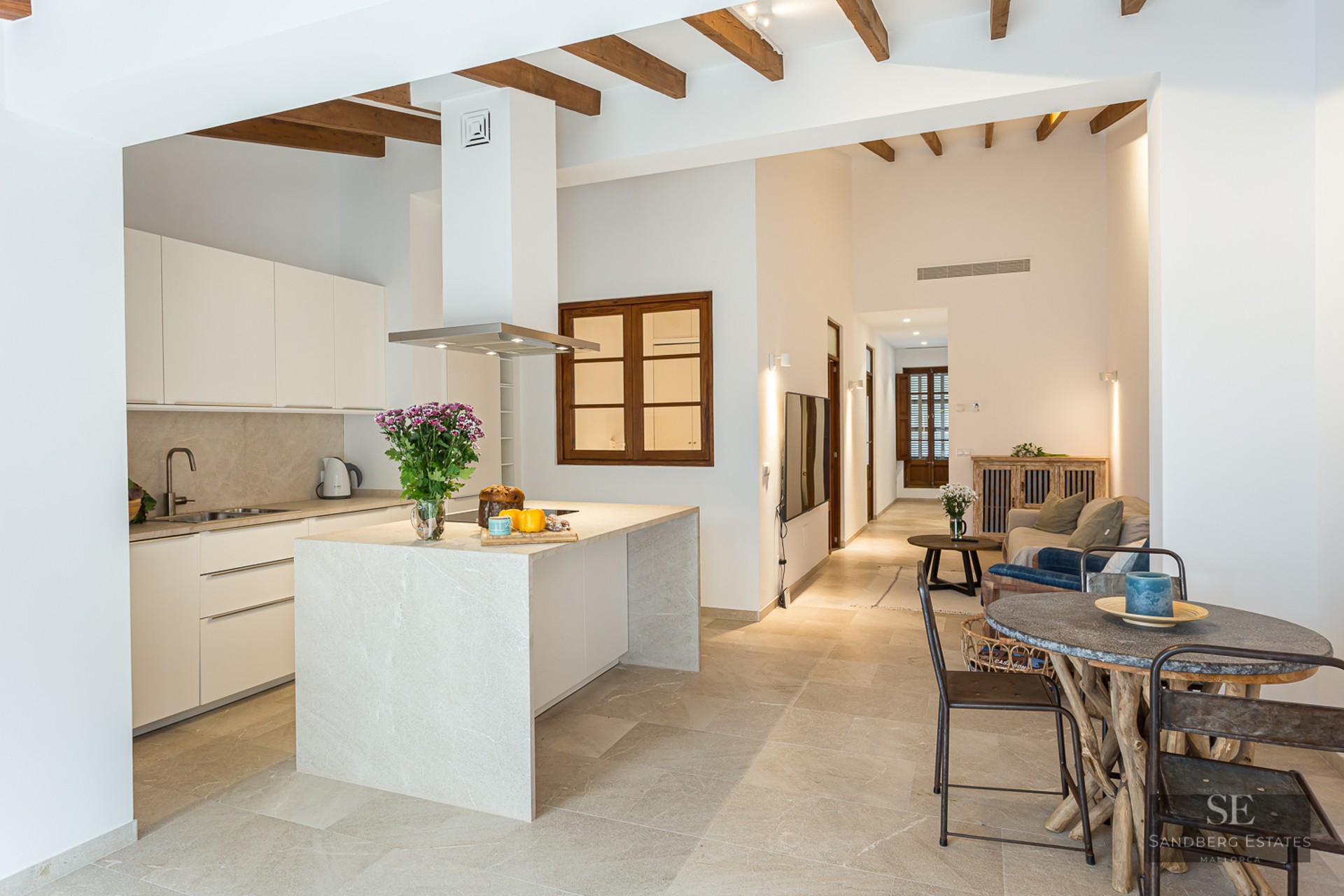 Bright open-plan kitchen featuring a stone island, wooden ceiling beams, and a rustic dining area.
