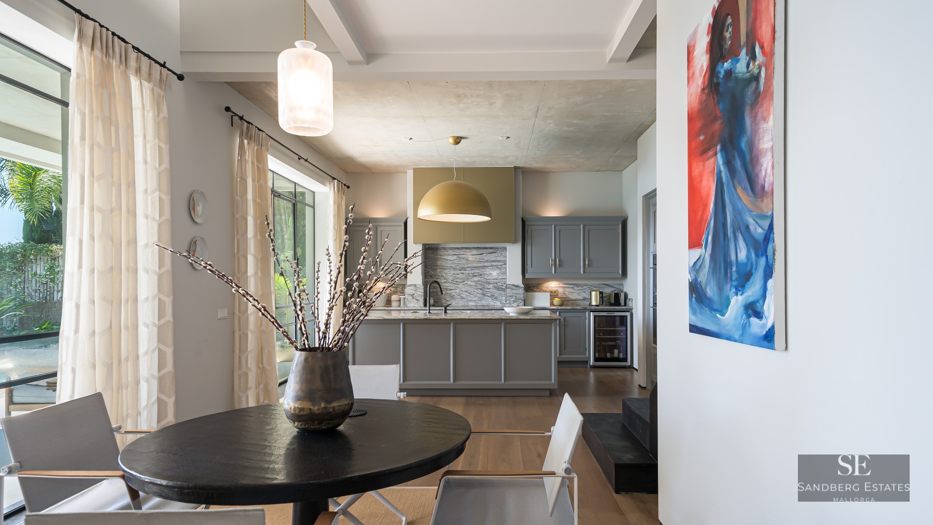 Modern kitchen with grey island, marble backsplash, gold lamp, and dining table with chairs by a large window.
