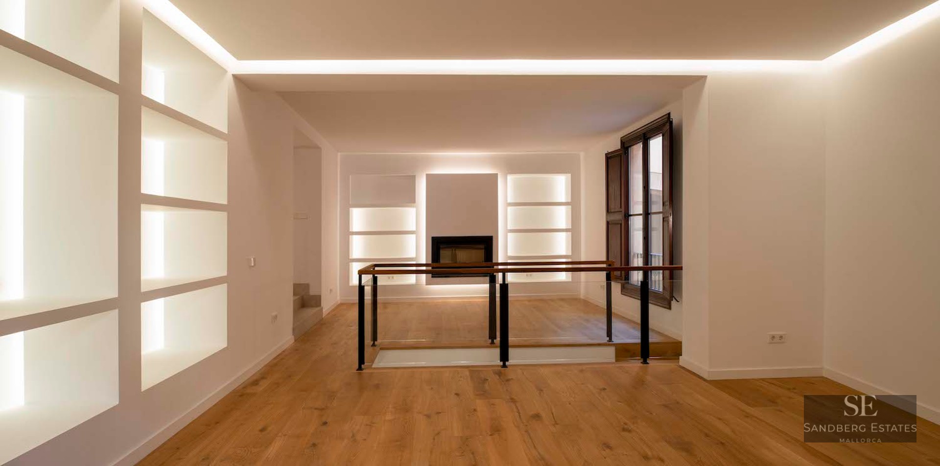 Minimalist interior with light oak floors, white walls featuring LED-lit niches, and a glass-railed staircase landing.