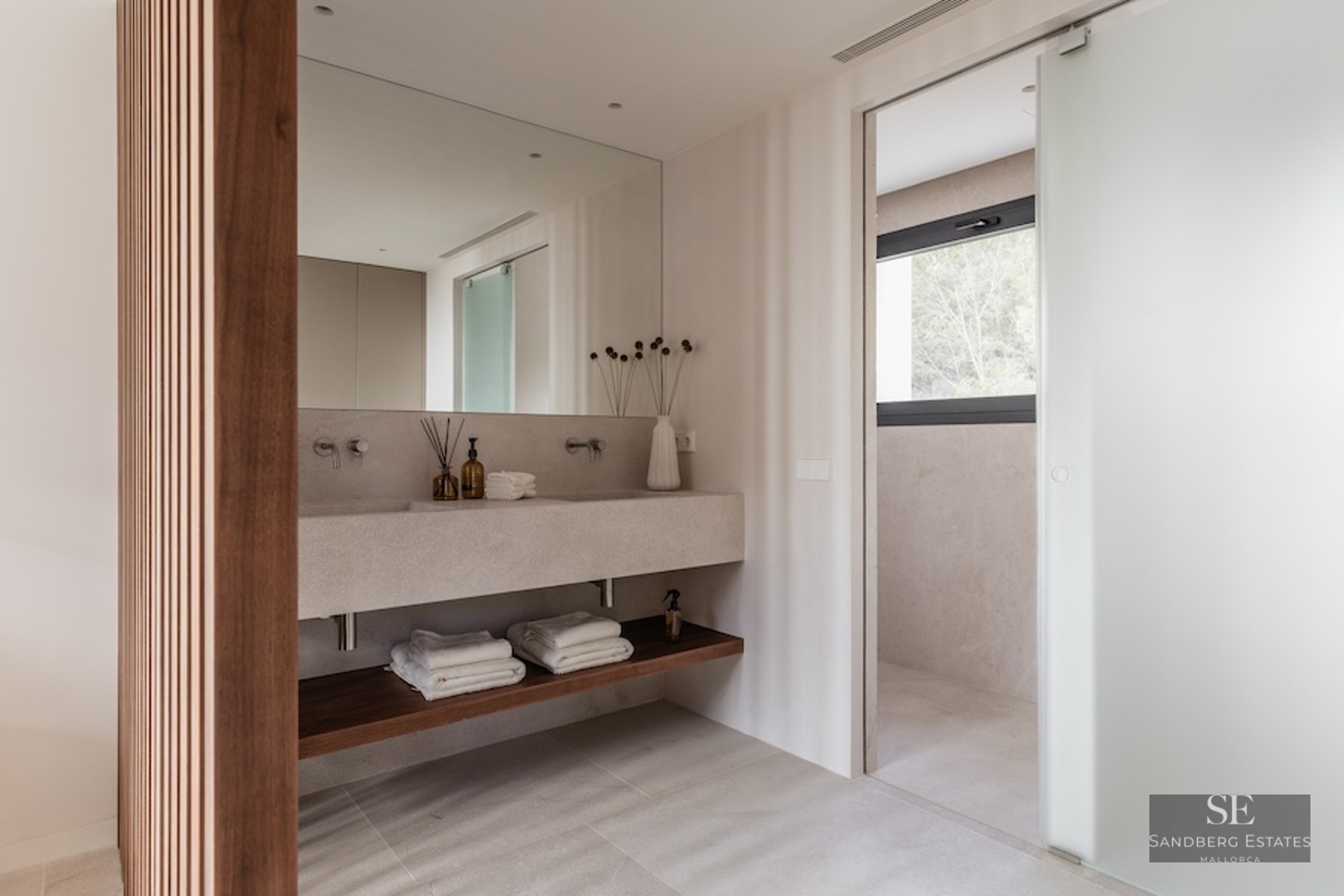 Modern master bathroom featuring a beige stone double vanity, wooden slat wall, and frosted glass sliding door.