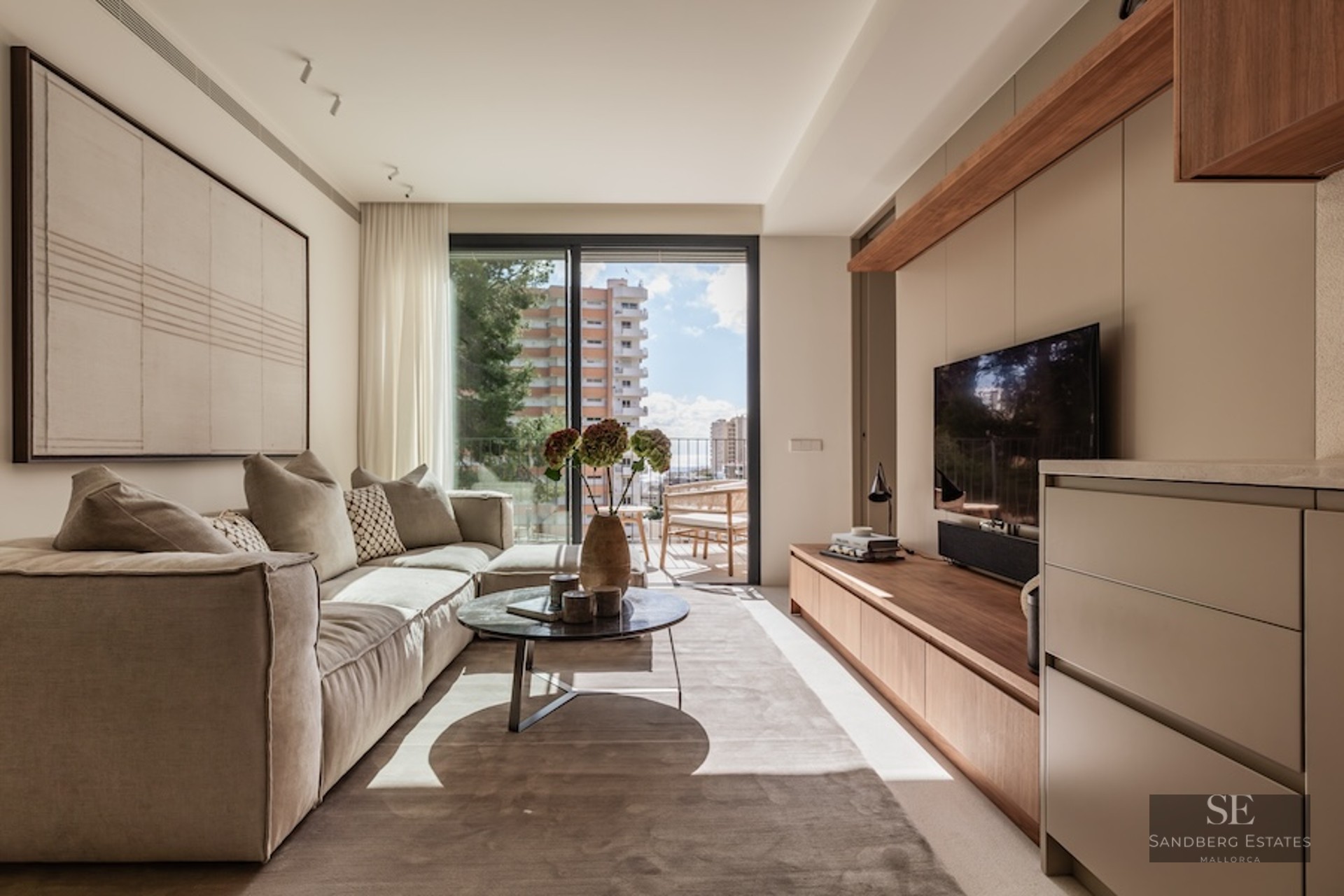 Bright living room featuring a large beige sofa, marble coffee table, and floor-to-ceiling glass doors to a balcony.