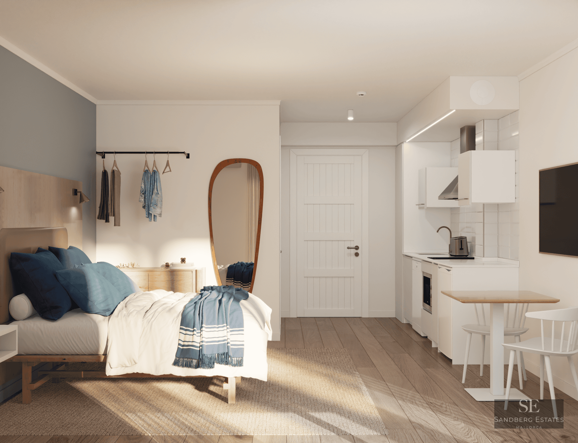 Studio lumineux avec lit aux accents bleus, grand miroir et kitchenette blanche moderne.