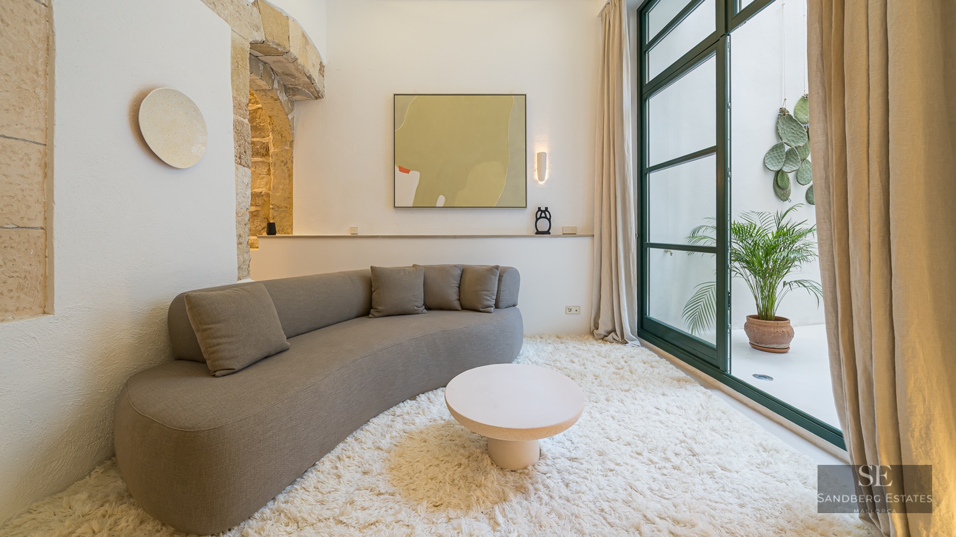 Modern curved sofa on a white shag rug in a room featuring a stone arch and patio access.