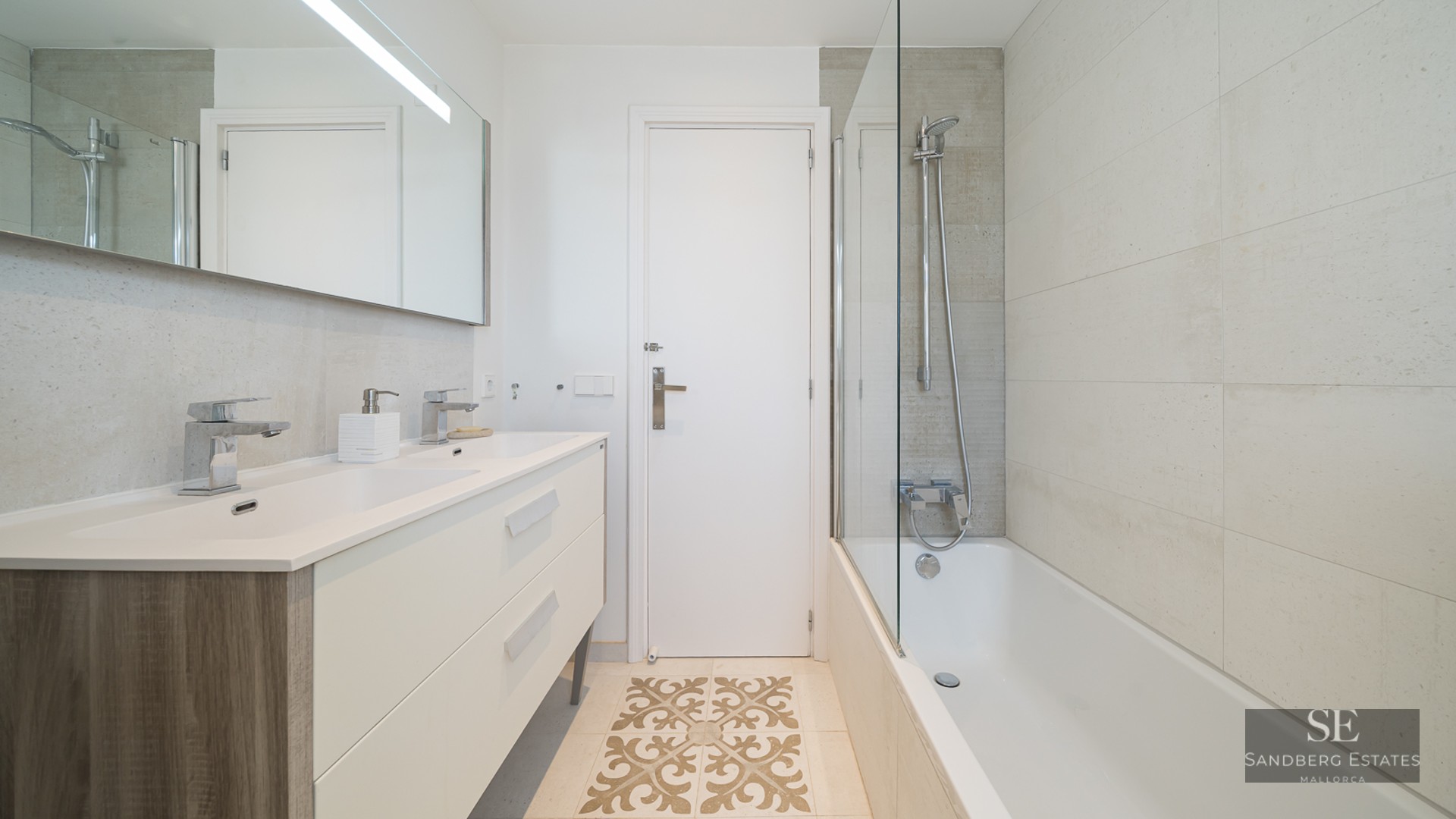 Modern bathroom featuring a cream double vanity, bathtub with glass screen, and decorative floor tile detail.