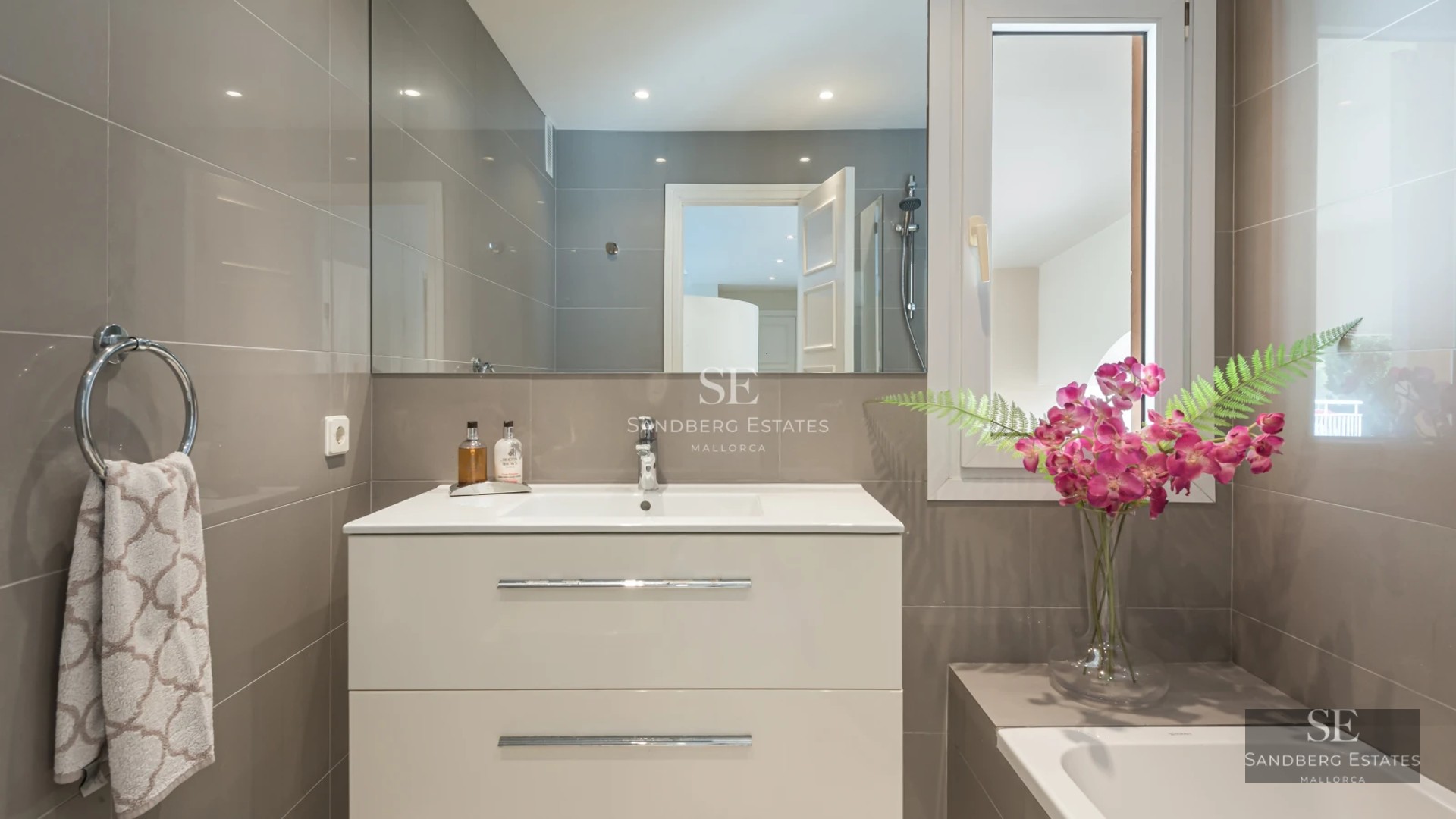 View of a modern villa with an infinity pool, large windows, and minimalist design. Well-maintained garden and clear sky.