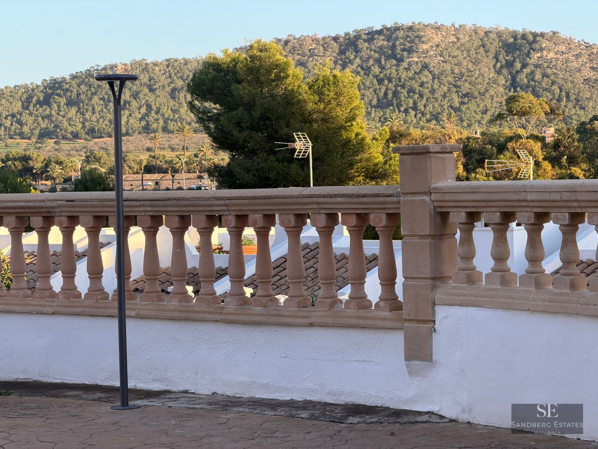 A stone balustrade on a white terrace overlooking a lush green mountain under a clear sky.