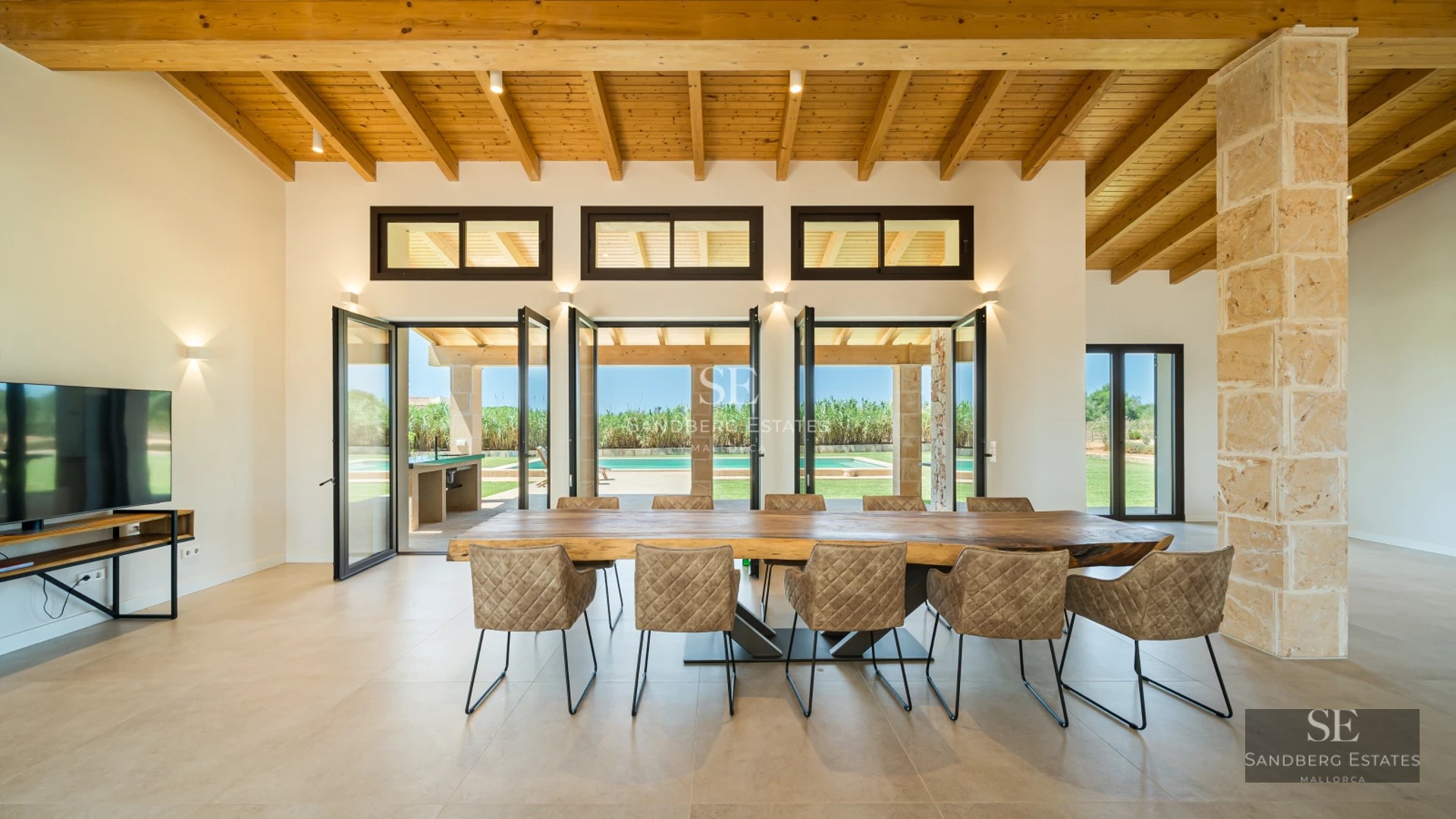 Bright living room with grey sofas, wooden coffee table, and large windows offering exterior views. Minimalist and elegant design.
