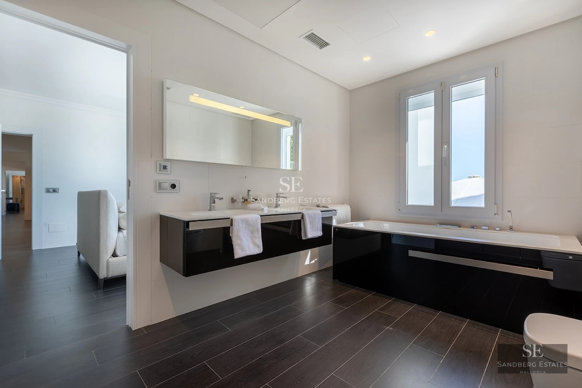 Spacious modern bathroom featuring a black and white double vanity, large mirror, and a bathtub with dark floor tiles.
