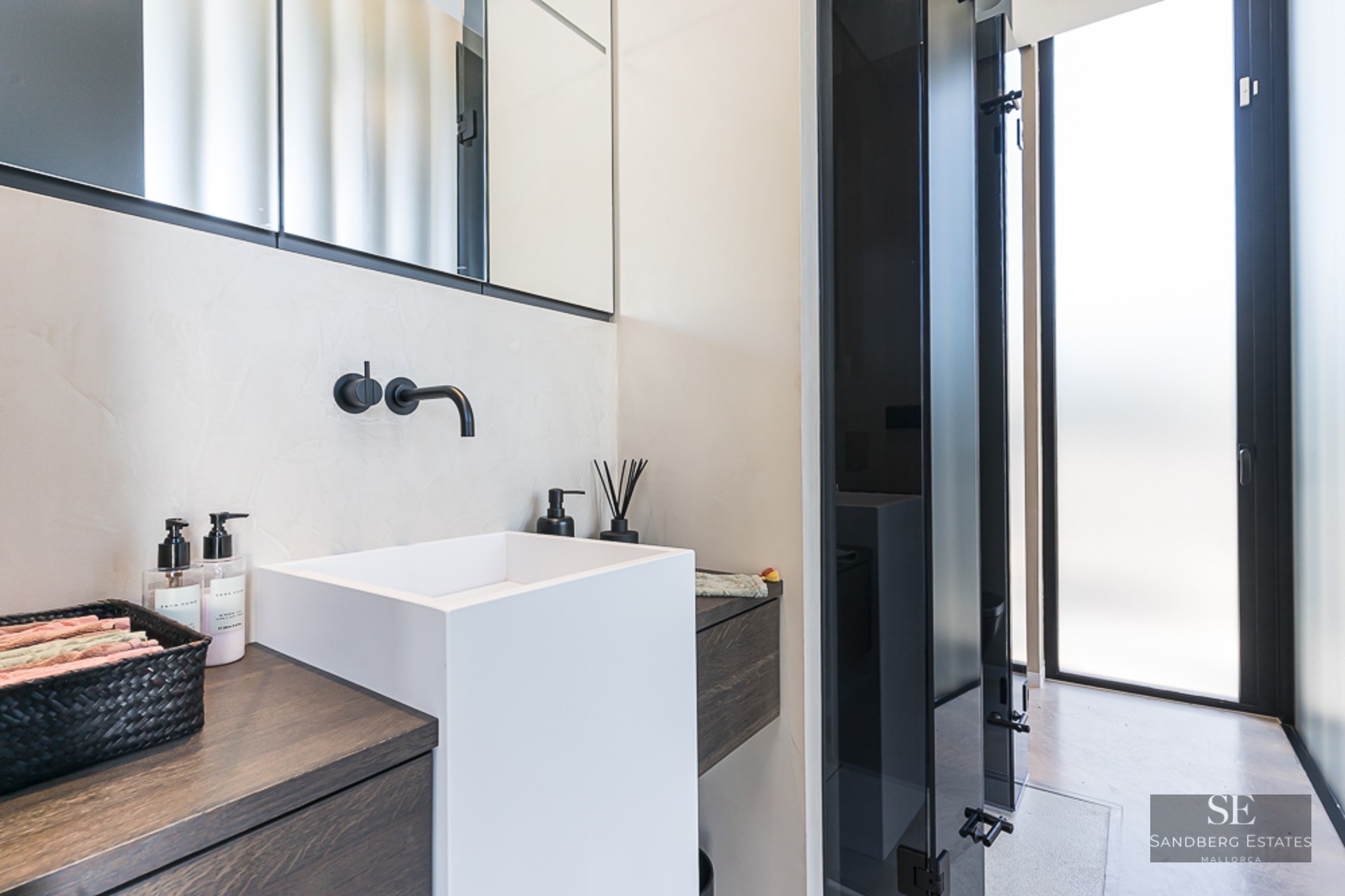 White square vessel sink with matte black wall-mounted faucet on dark wood vanity in a modern bathroom.