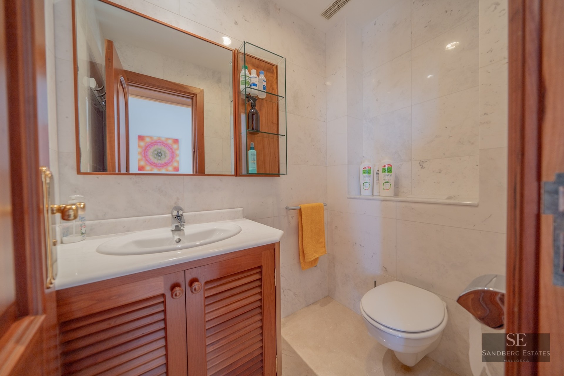 Bathroom featuring marble walls, a wooden vanity unit, a large mirror, and a white toilet.