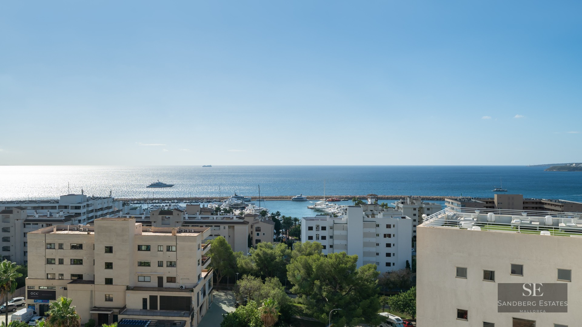 High-angle view of a coastal city, a yacht-filled marina, and the vast blue Mediterranean Sea under a bright sky.