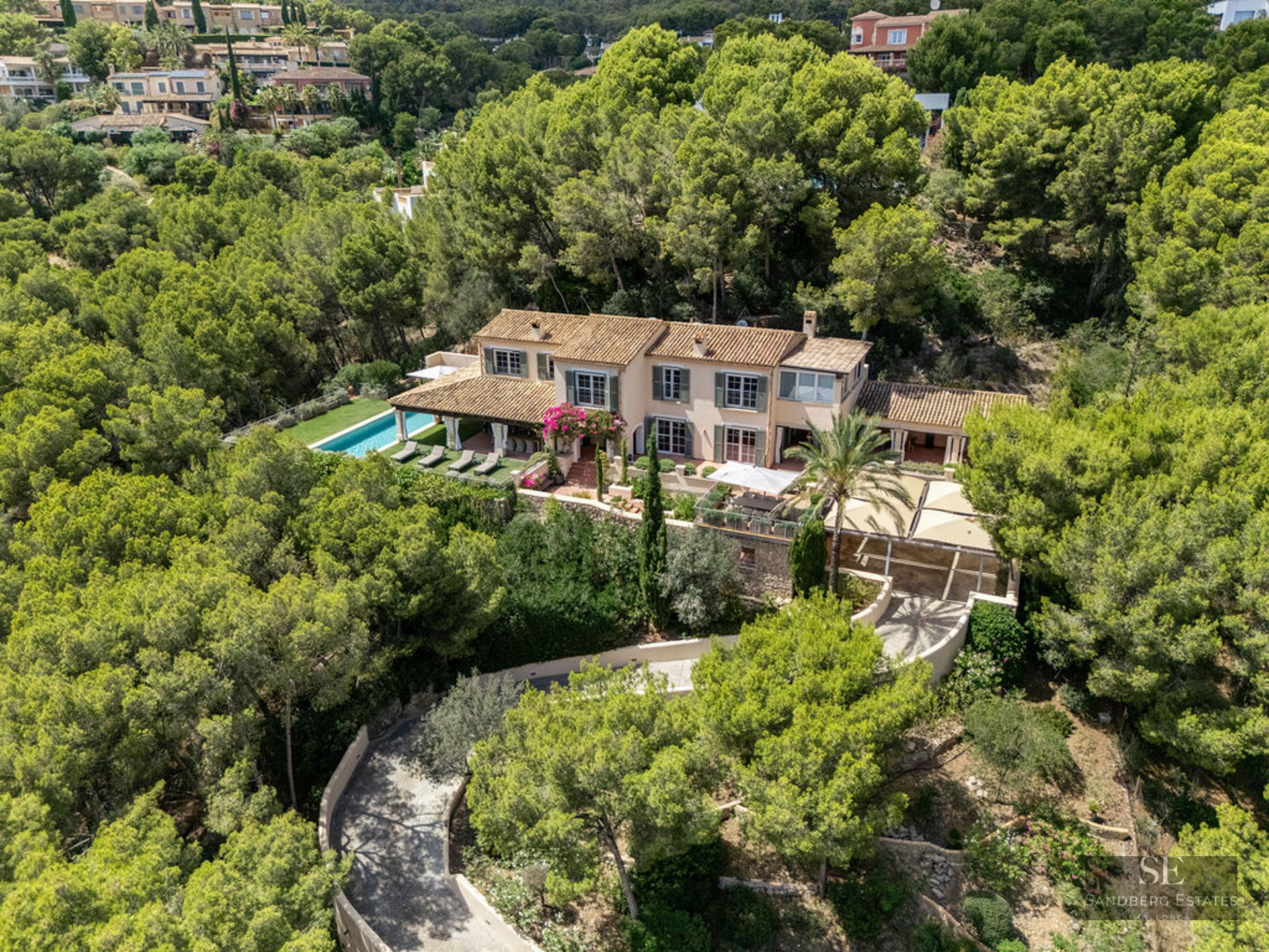 Aerial shot of a luxury Mediterranean villa with a pool, terracotta roof, and lush green forest surroundings.