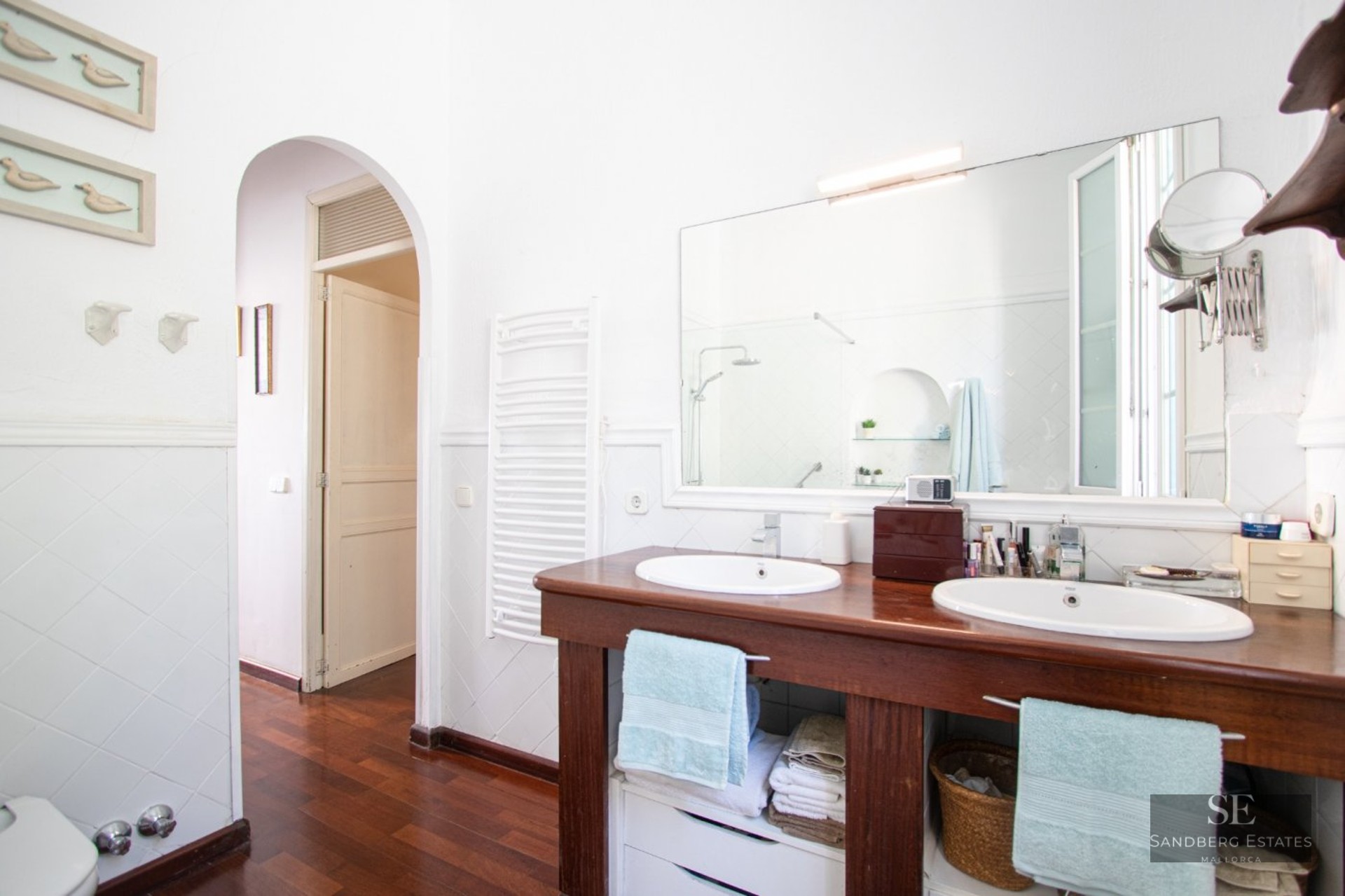 Bathroom featuring a wooden double vanity with two white sinks, a large mirror, and dark wood floors.