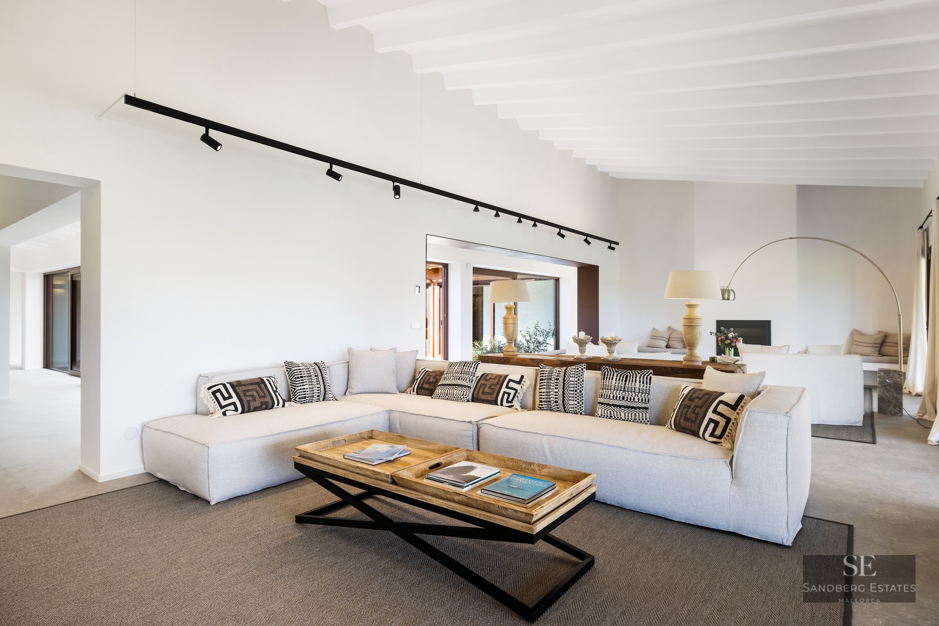 Spacious living room featuring a large grey sectional sofa, geometric cushions, and wooden coffee table under a white beamed ceiling.