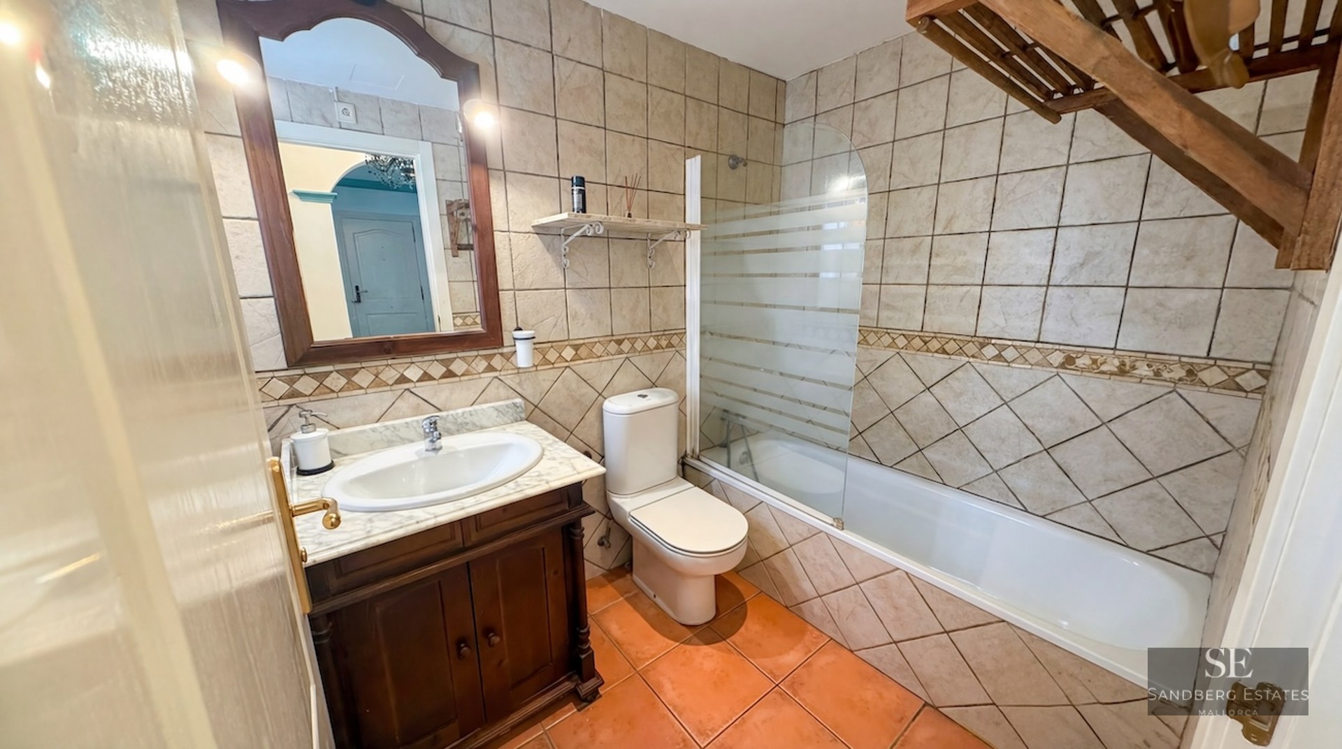 Bathroom featuring a bathtub, toilet, marble-top vanity, and earth-toned ceramic tiling.