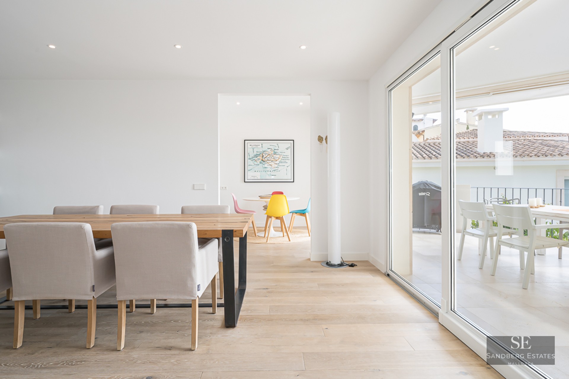 Salle à manger spacieuse avec table en bois, chaises beiges et baies vitrées ouvrant sur une terrasse.