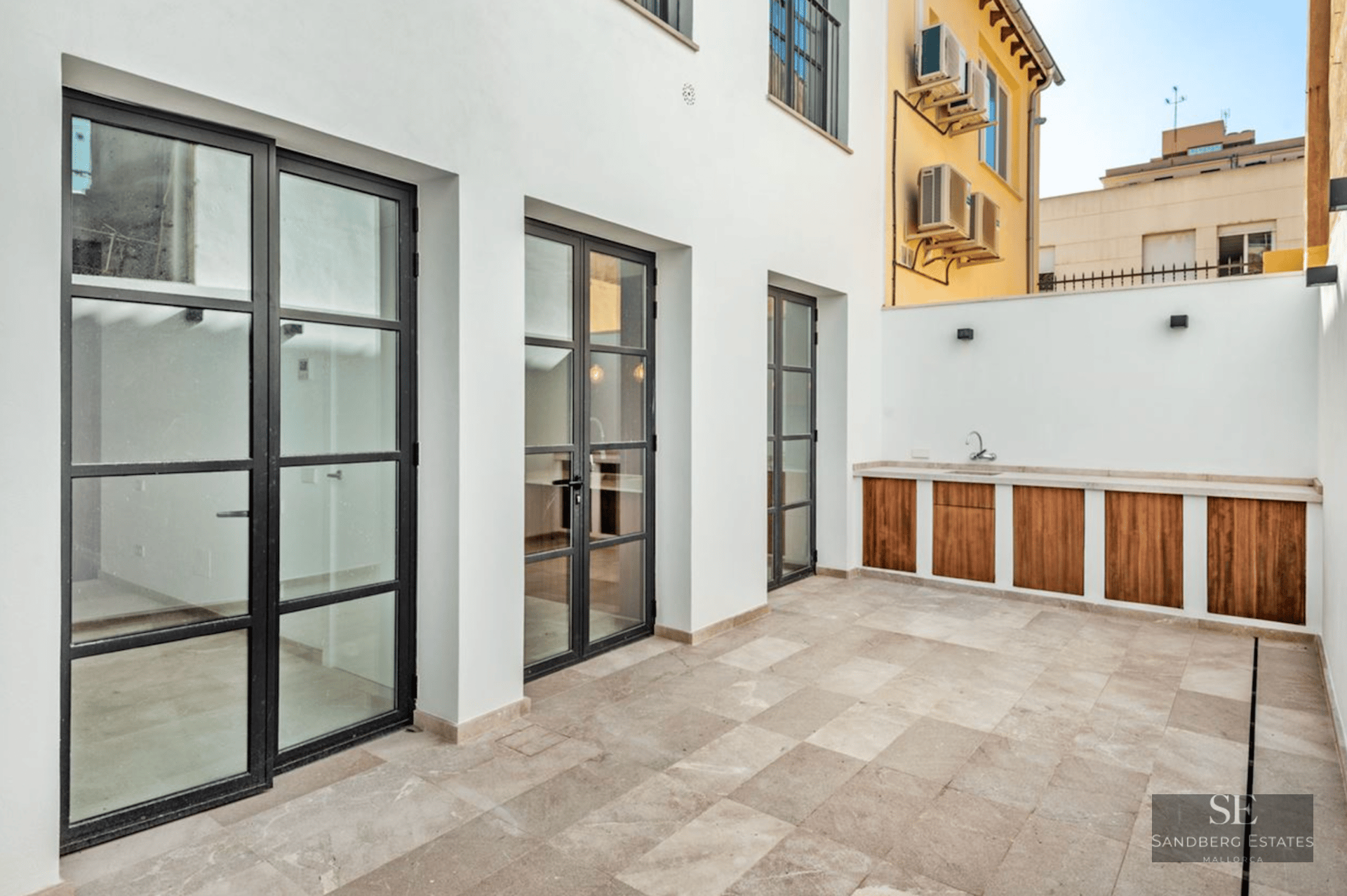 Modern terrace featuring stone tiling, black industrial glass doors, and a wood-accented outdoor kitchen unit.