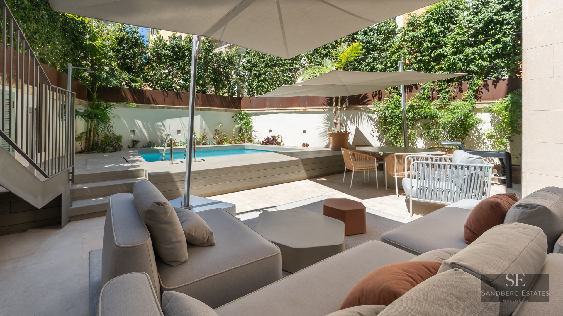 Sun-drenched terrace featuring a private pool, modern grey sofas with terracotta pillows, and large white umbrellas.