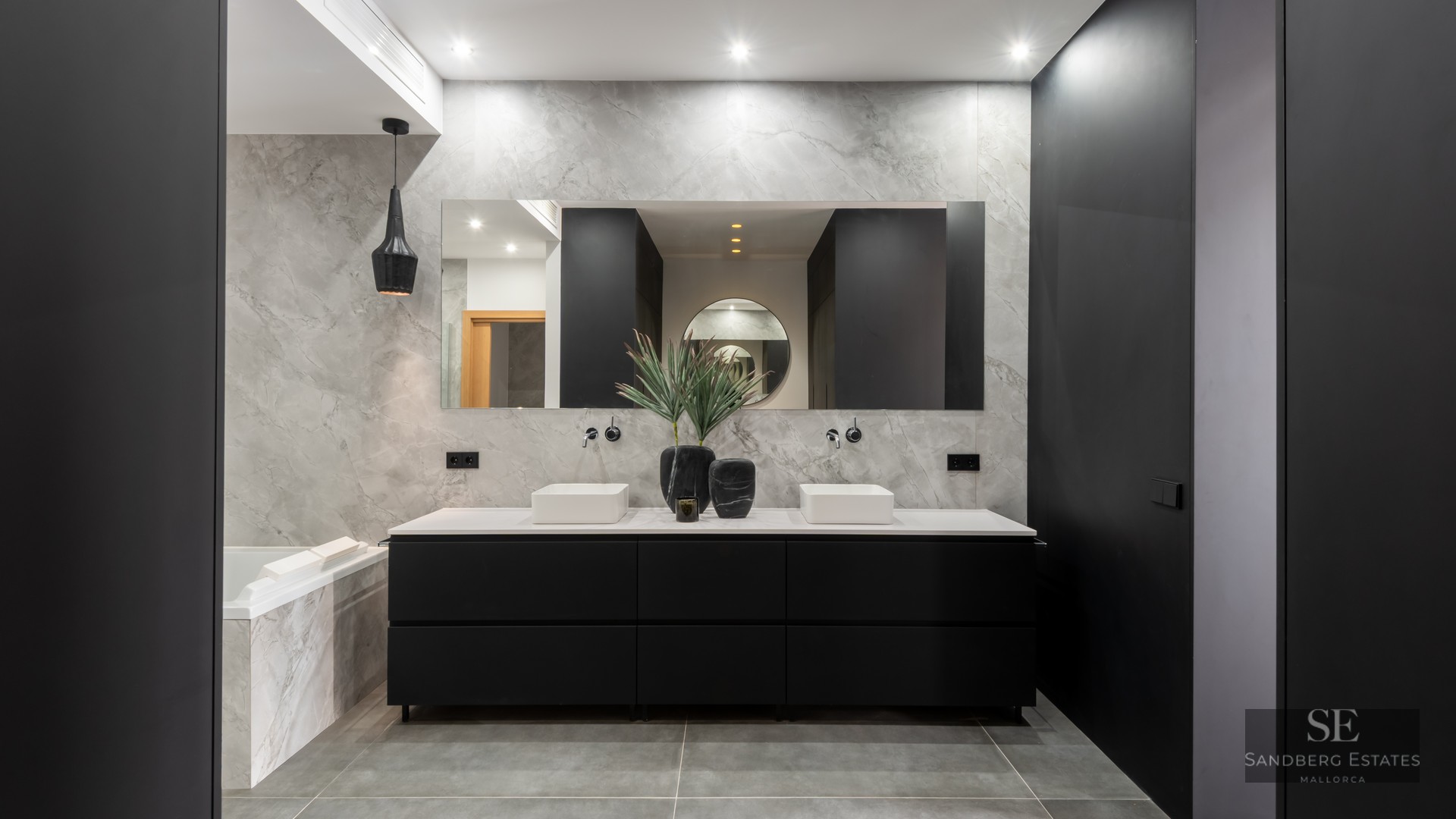 Luxury bathroom with marble walls, double white basins on a black vanity unit, and a large mirror.