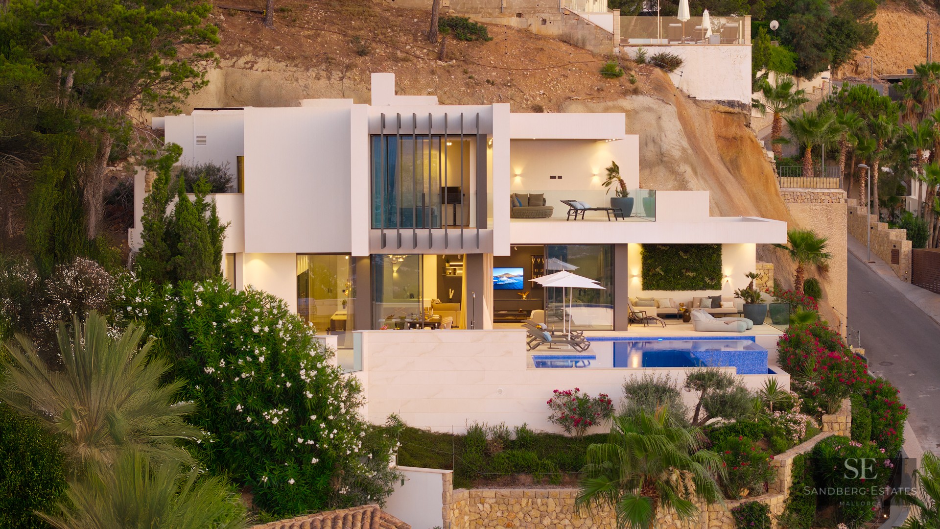 Modern white multi-level villa with a swimming pool, terraces, and large glass windows built into a rocky hillside.