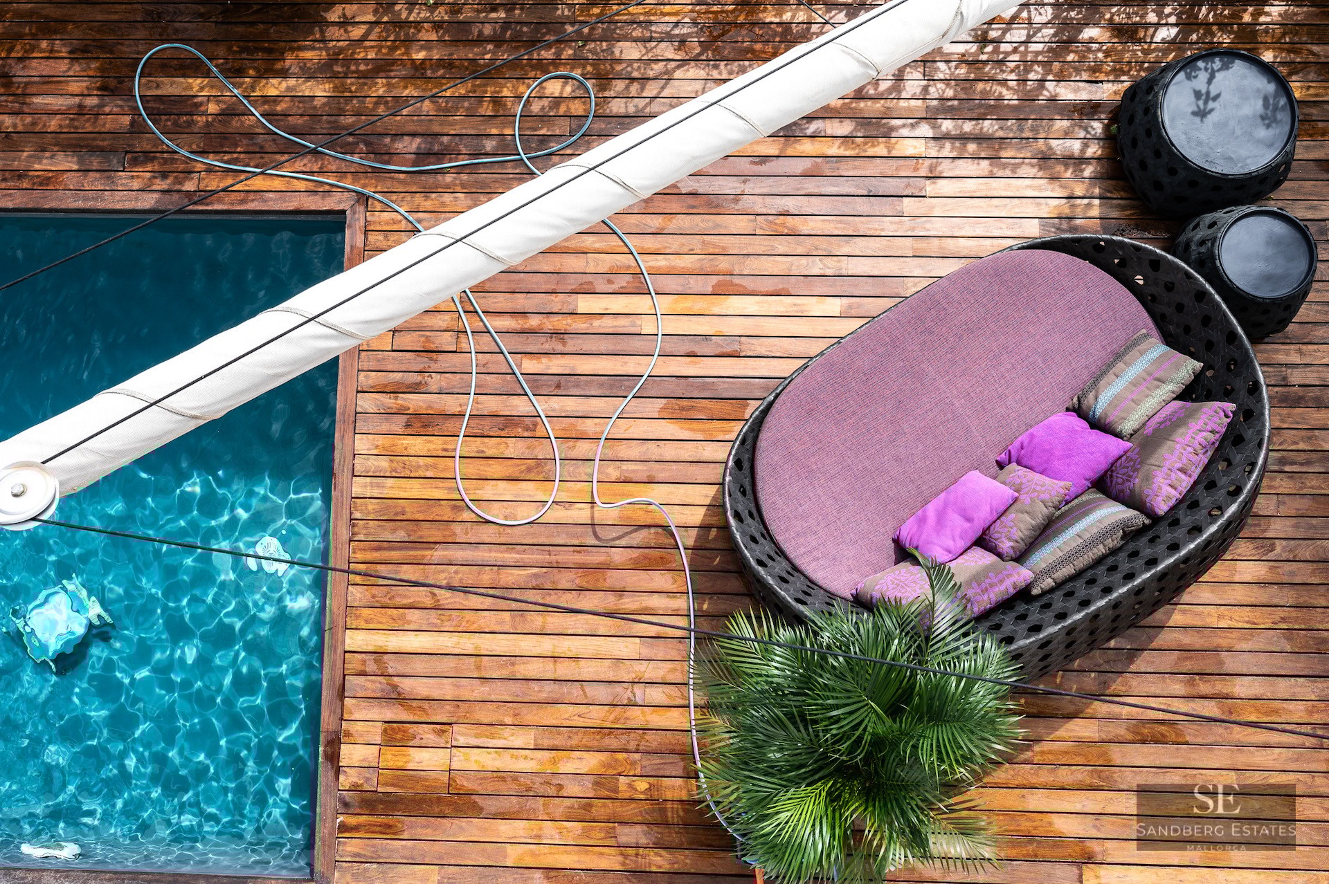 Overhead view of a turquoise pool next to a wooden deck with a large circular purple lounge chair.