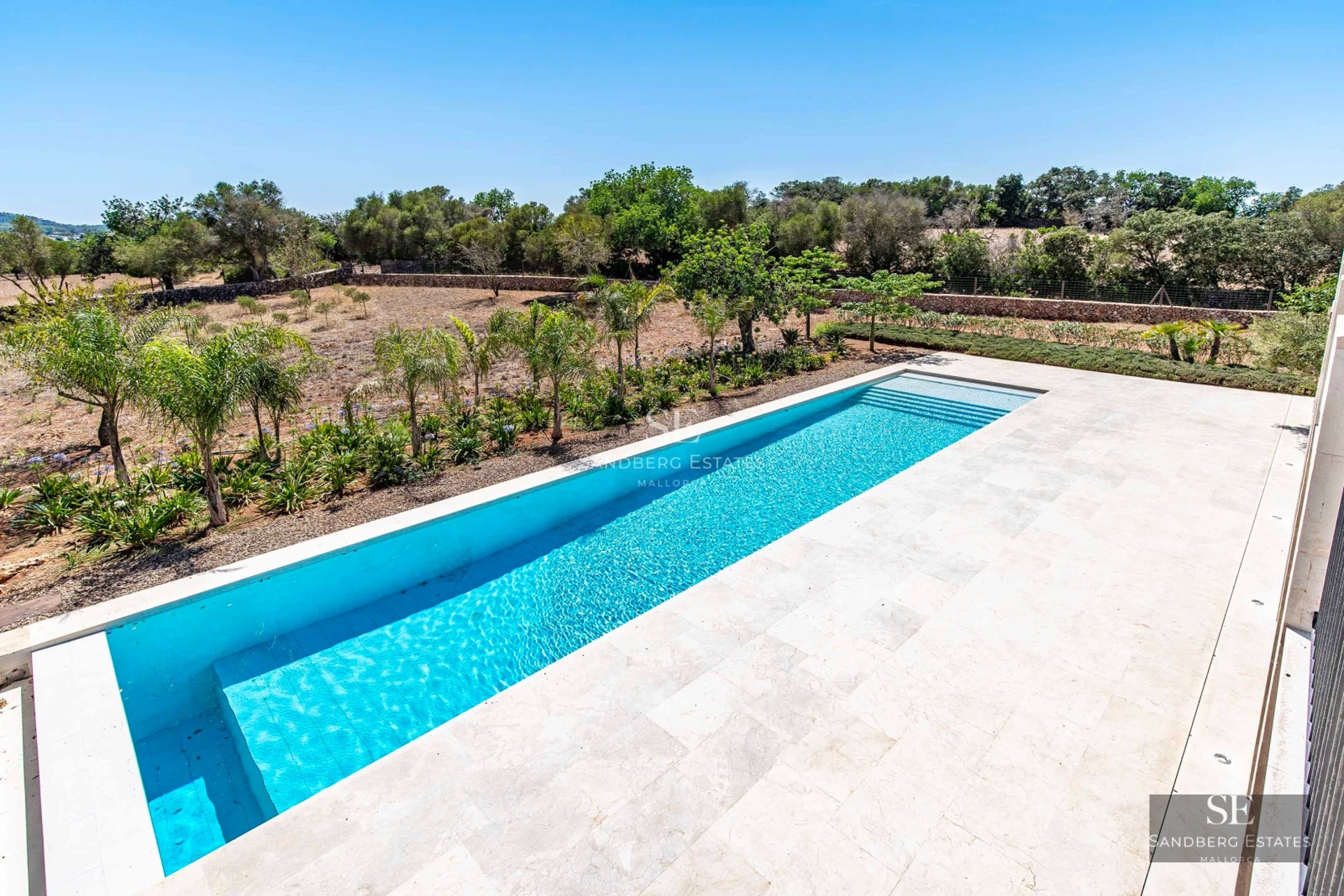 Bright, spacious living room with panoramic windows, light wood flooring, and modern designer furniture. Views of a lush garden.