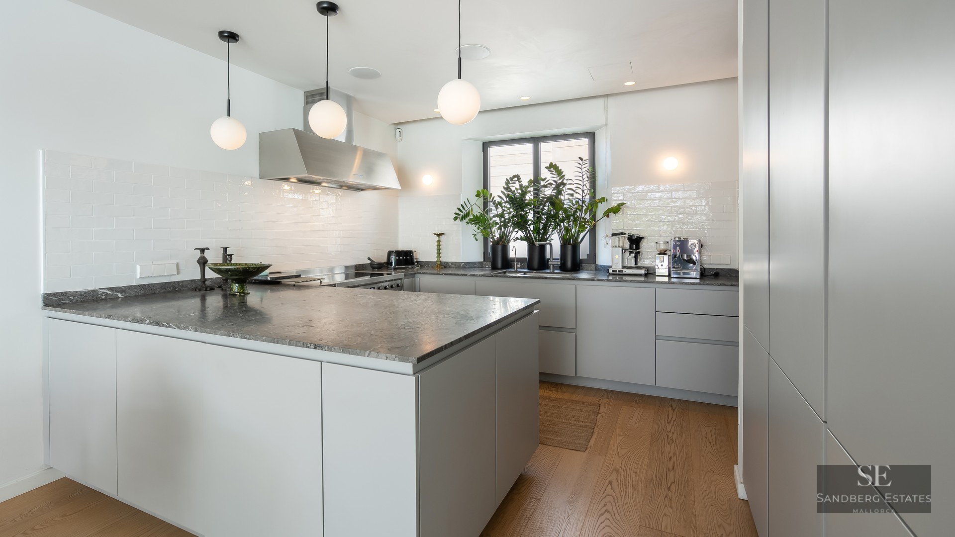 Contemporary kitchen featuring a large gray marble island, minimalist gray cabinetry, and white globe pendant lights.