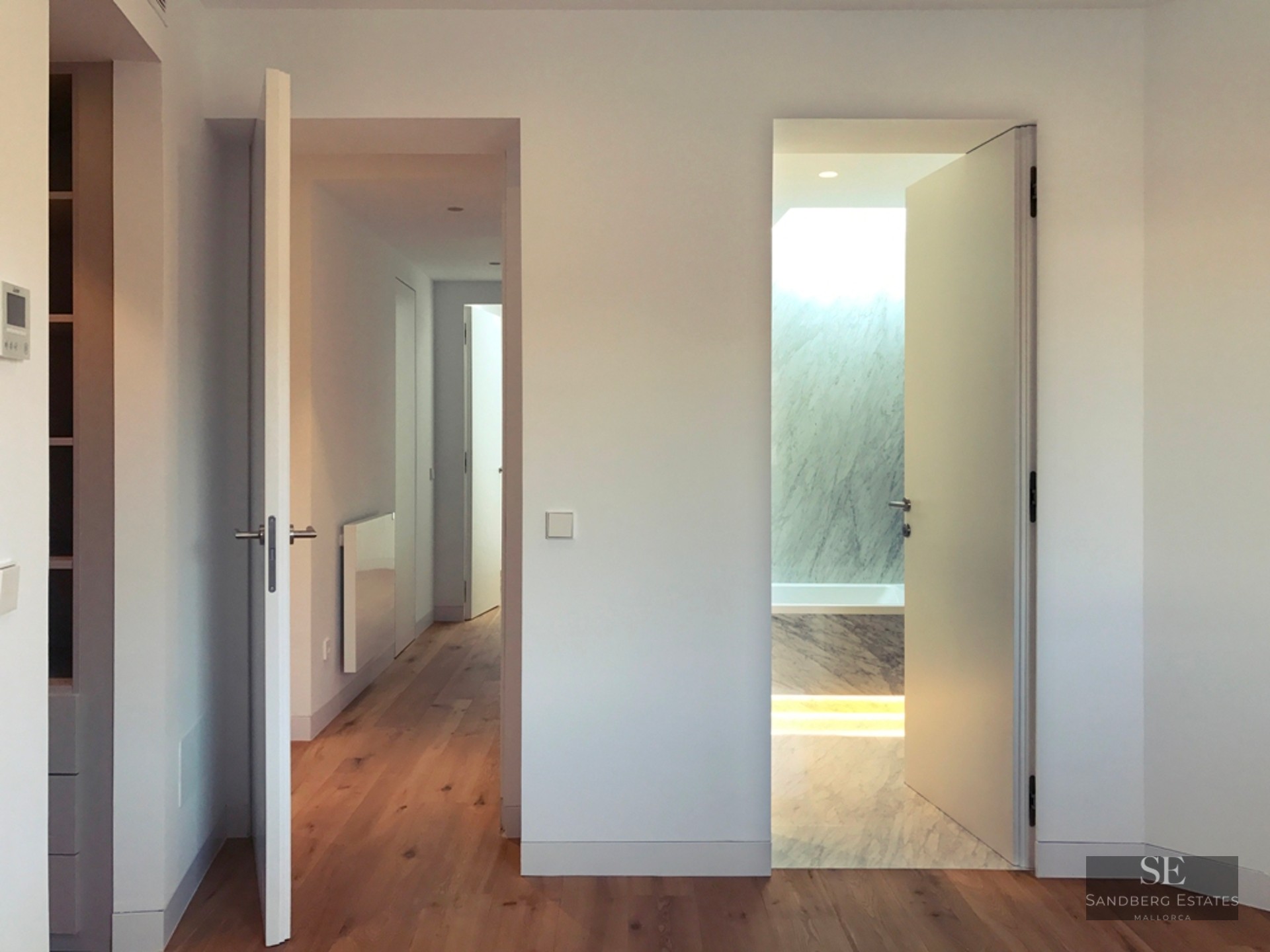 Interior view from a bedroom showing a hallway to the left and an open door to a white marble ensuite bathroom.